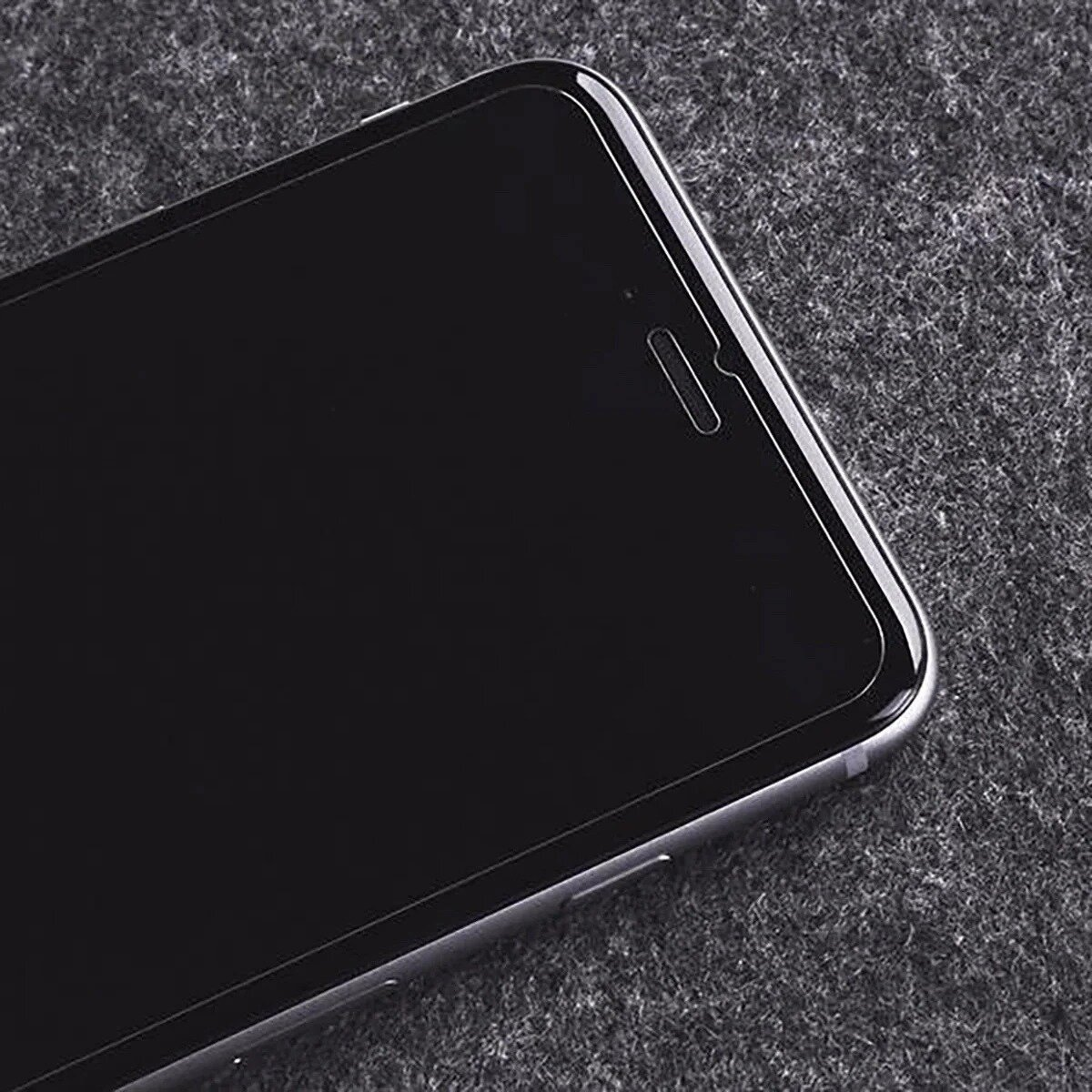 Een zwarte smartphone op een grijze, getextureerde ondergrond. Het scherm is donker en heeft een inkeping aan de bovenkant.