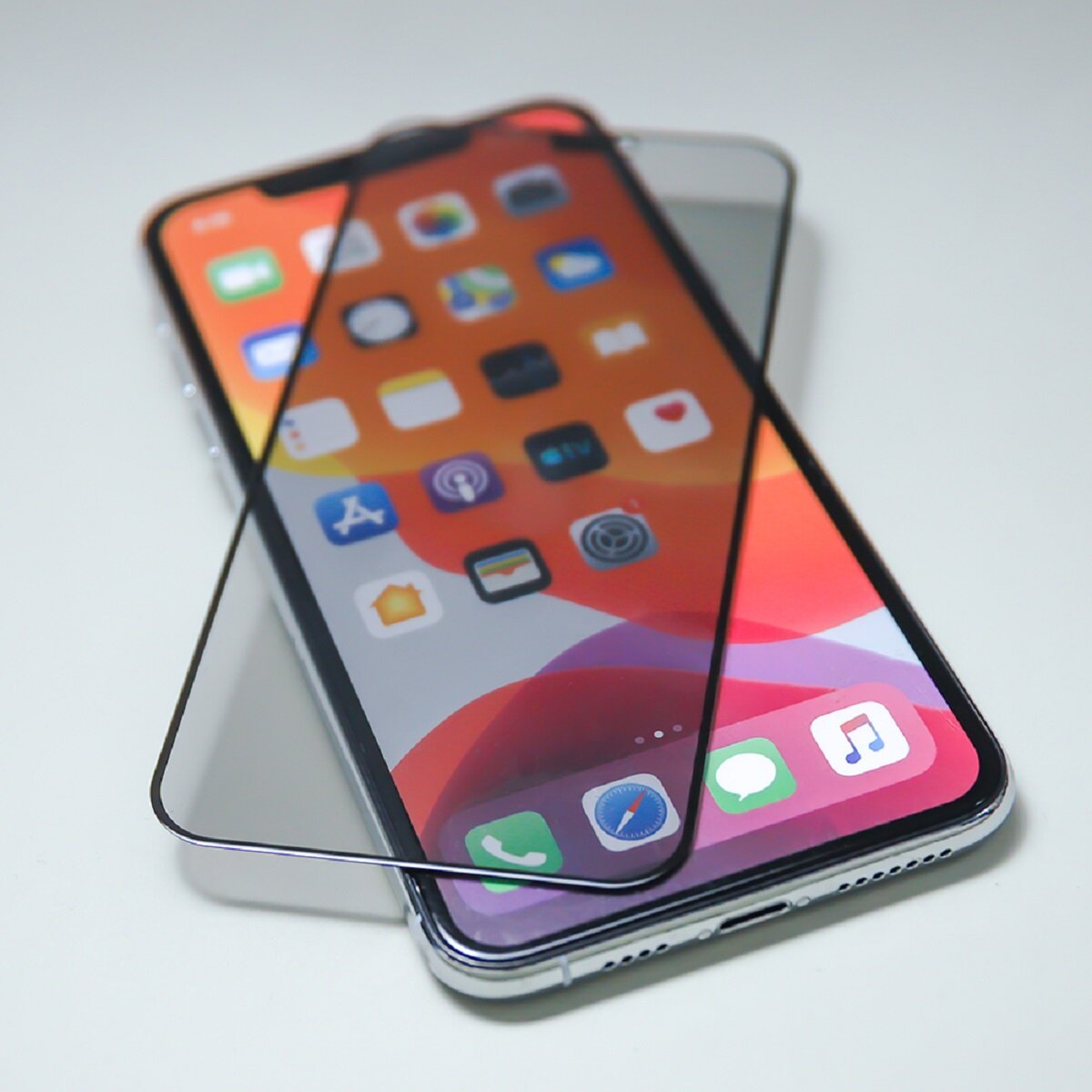 Un iPhone avec protecteur d'écran. L'écran affiche des icônes d'applications. Le téléphone est sur une surface blanche.