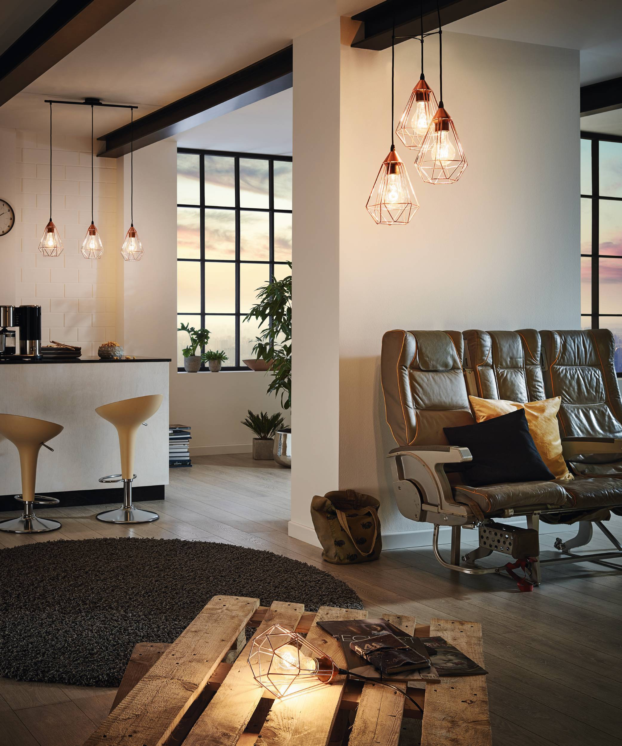Ein modernes Interieur mit Hängelampen, Ledersofa, Pflanzen und einem Palettentisch. Die Szene ist gut beleuchtet.