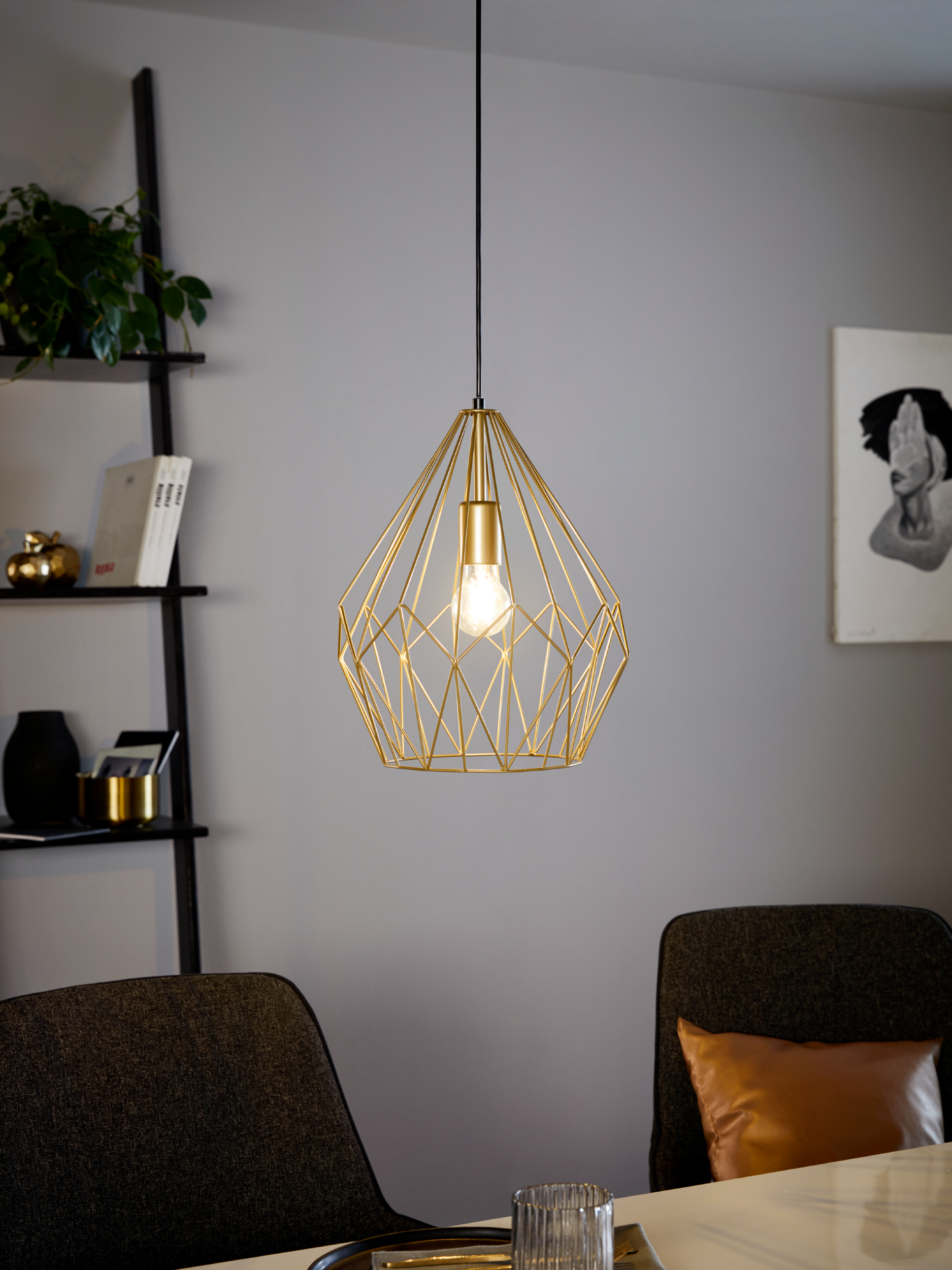 Goldene geometrische Pendelleuchte. Esszimmer mit Stühlen, Kunst und einem schwarzen Regal mit Dekoration.