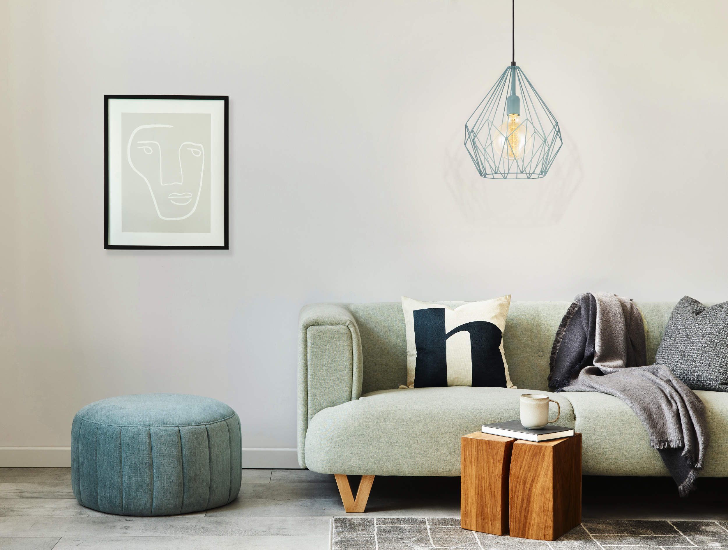 Ein Wohnzimmer mit Sofa, Ottoman, Kunst und Pendelleuchte. Farben sind Türkis, Grau und Holztöne.