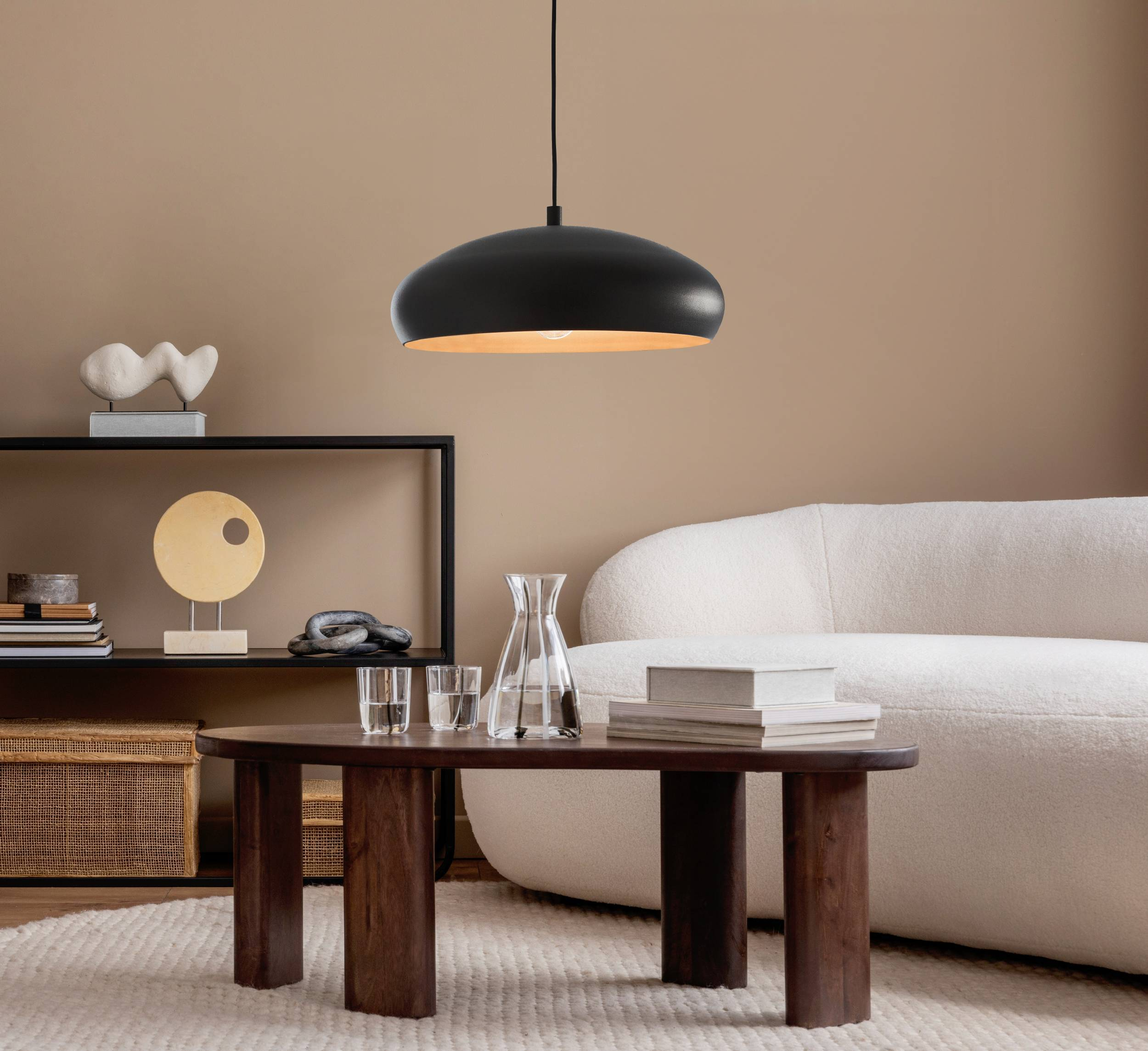 Ein Wohnzimmer mit schwarzer Pendelleuchte, Holztisch, weißem Sofa und dekorativen Elementen.