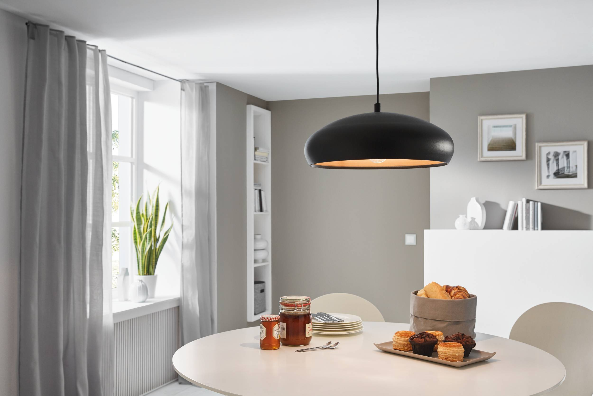 Ein Esszimmer mit rundem Tisch, schwarzer Lampe, Fenster mit Vorhängen und Essen auf dem Tisch.
