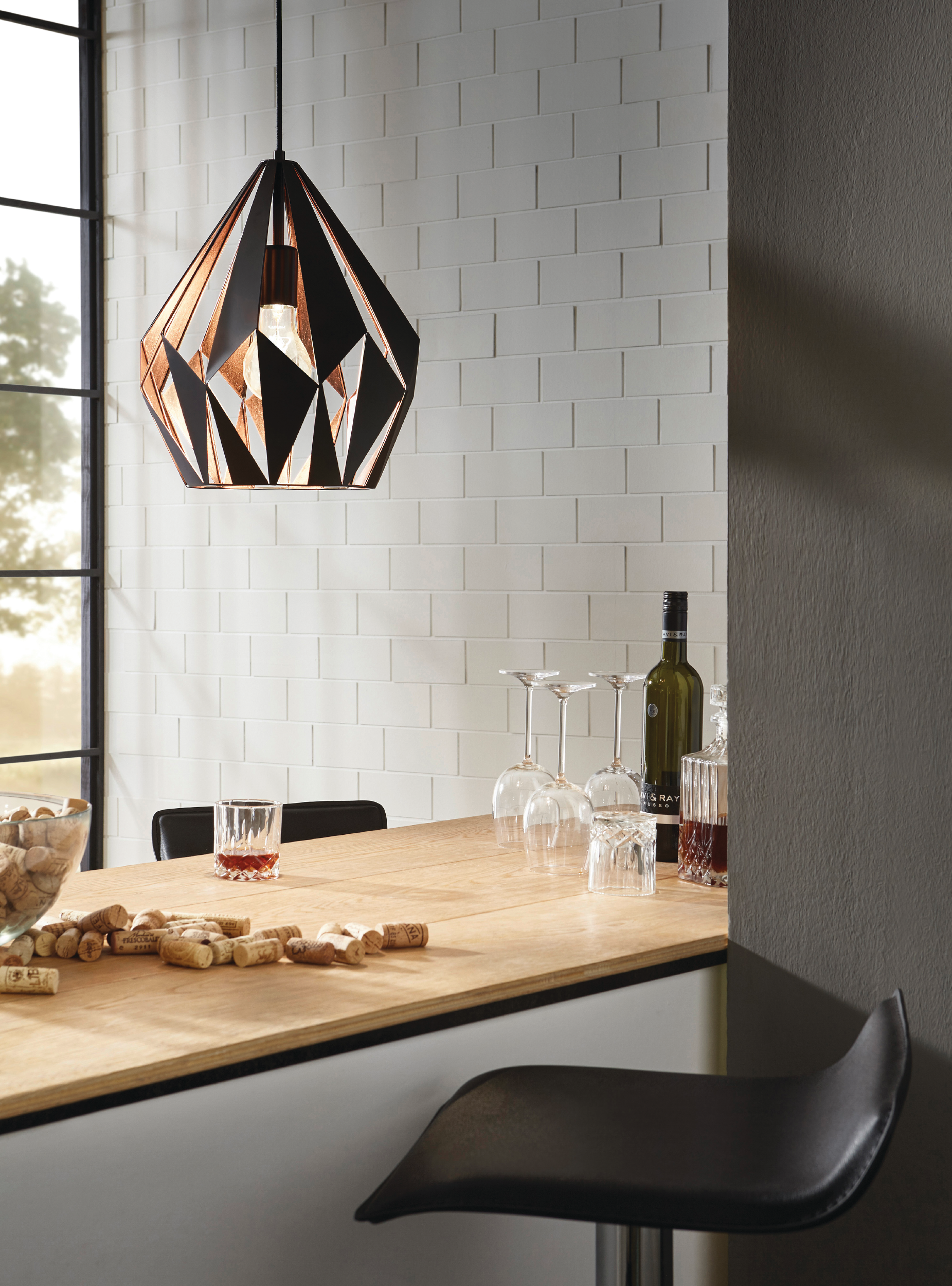 Ein Barbereich mit geometrischer Lampe, Weingläsern, Weinflaschen, einem Whiskyglas und Korken. Weiße Ziegelmauer.