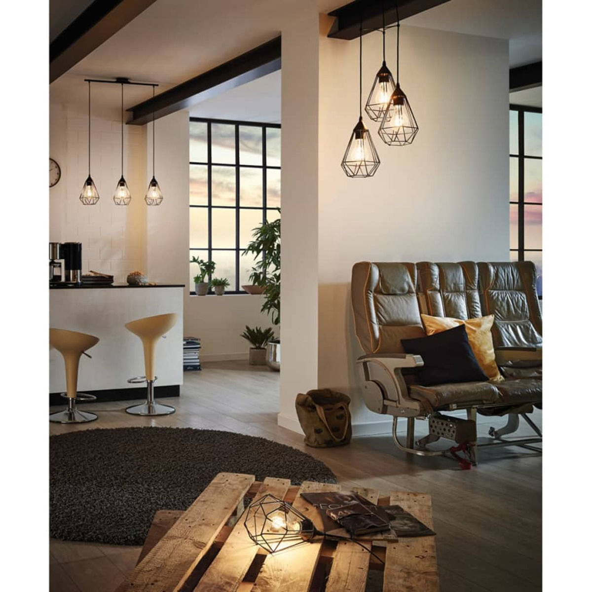 Interni con lampade a sospensione, divano in pelle, tavolo in legno e sgabelli da bar. Grandi finestre e piante sullo sfondo.