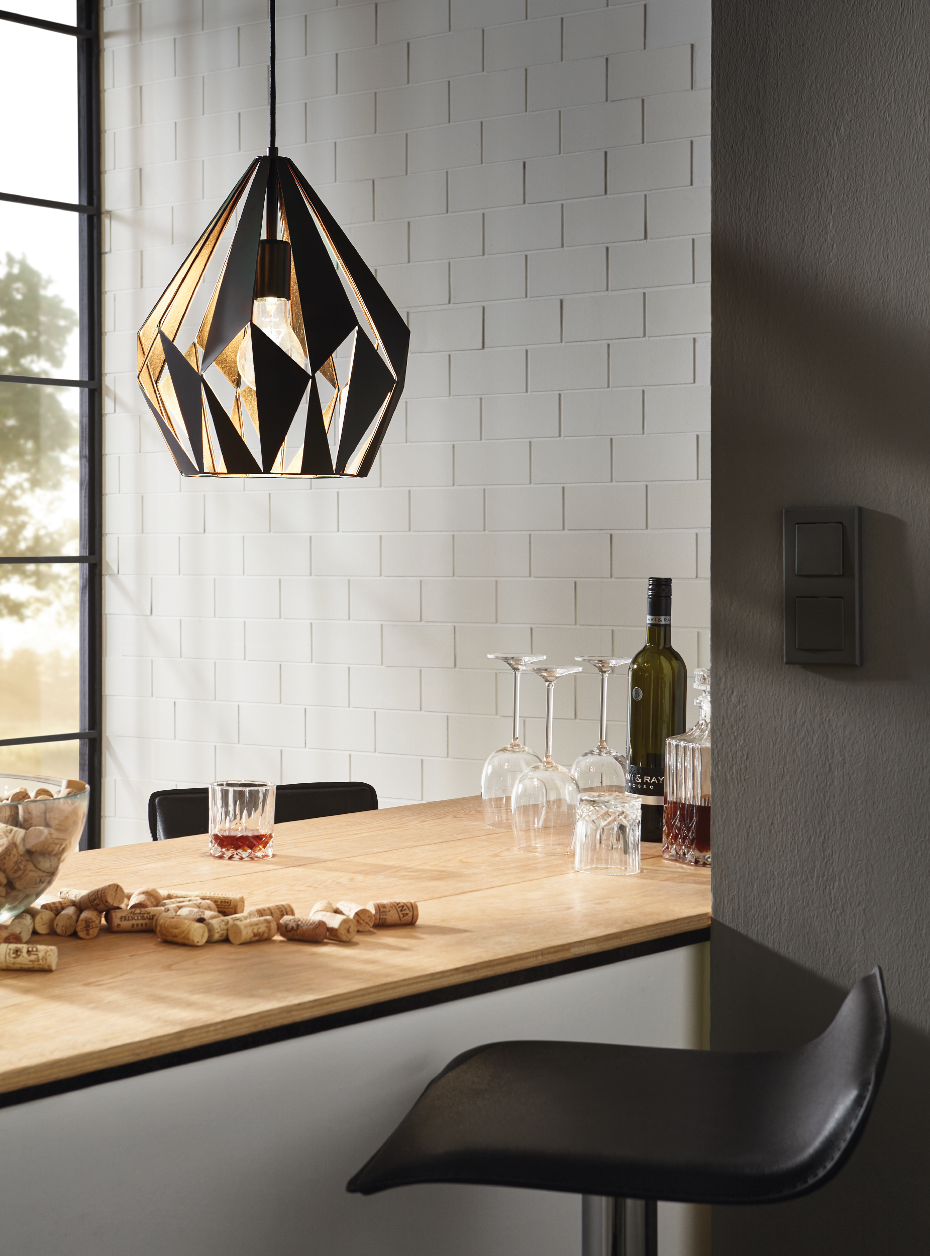Eine Küchenbar mit Weingläsern, einer Flasche, einem Glas Wein und Korken. Eine geometrische Lampe hängt darüber.