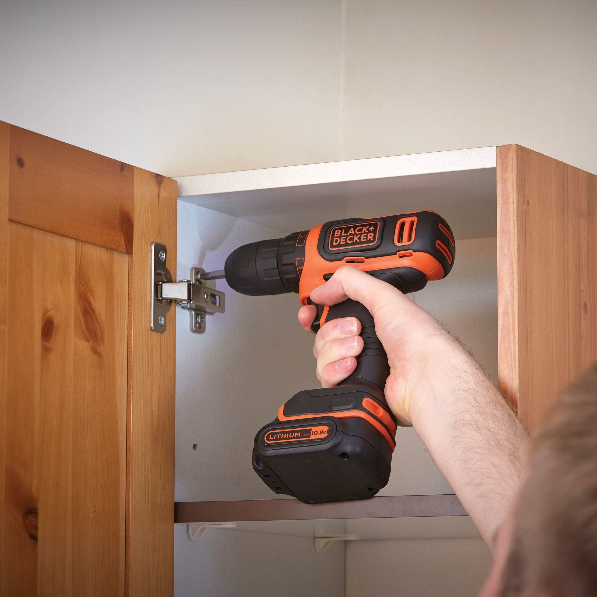 Una persona usa un trapano Black+Decker nero e arancione per installare una cerniera su un mobile in legno.