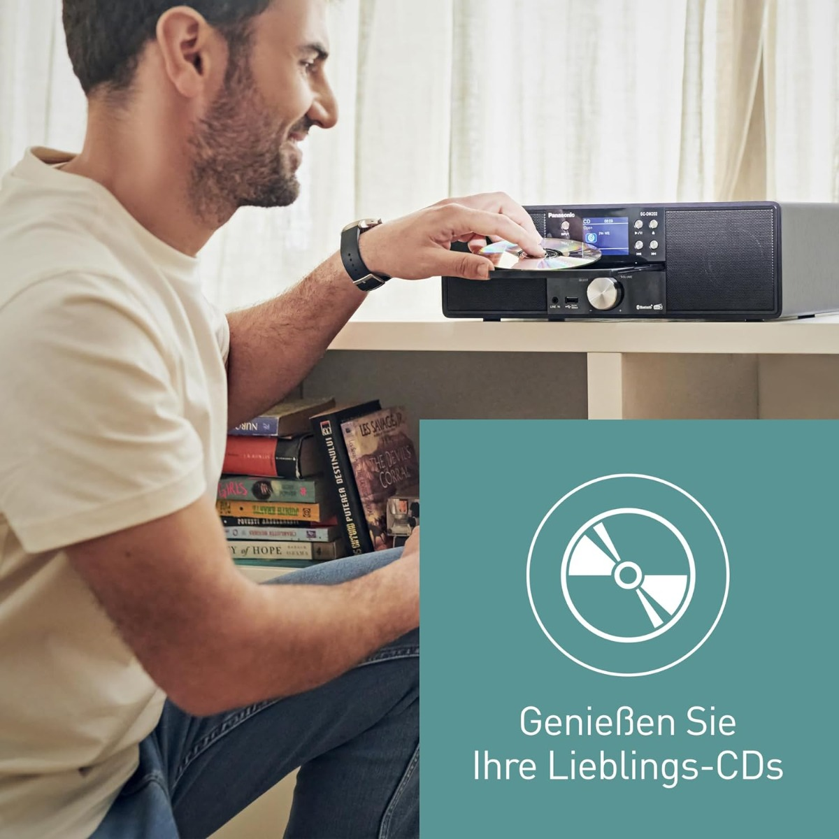 Ein Mann legt eine CD in eine schwarze Panasonic-Stereoanlage ein. Links sind Bücher gestapelt. Ein weißes Regal trägt die Anlage.