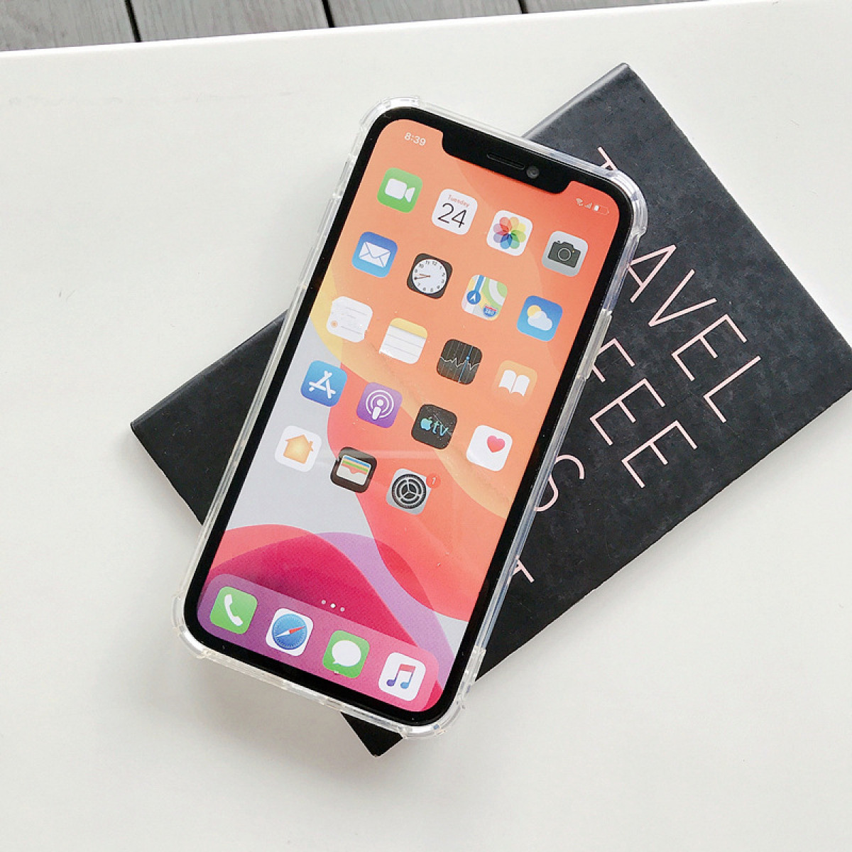 Un iPhone su un libro nero con testo bianco. Lo schermo del telefono mostra icone di app su uno sfondo rosa e arancione.