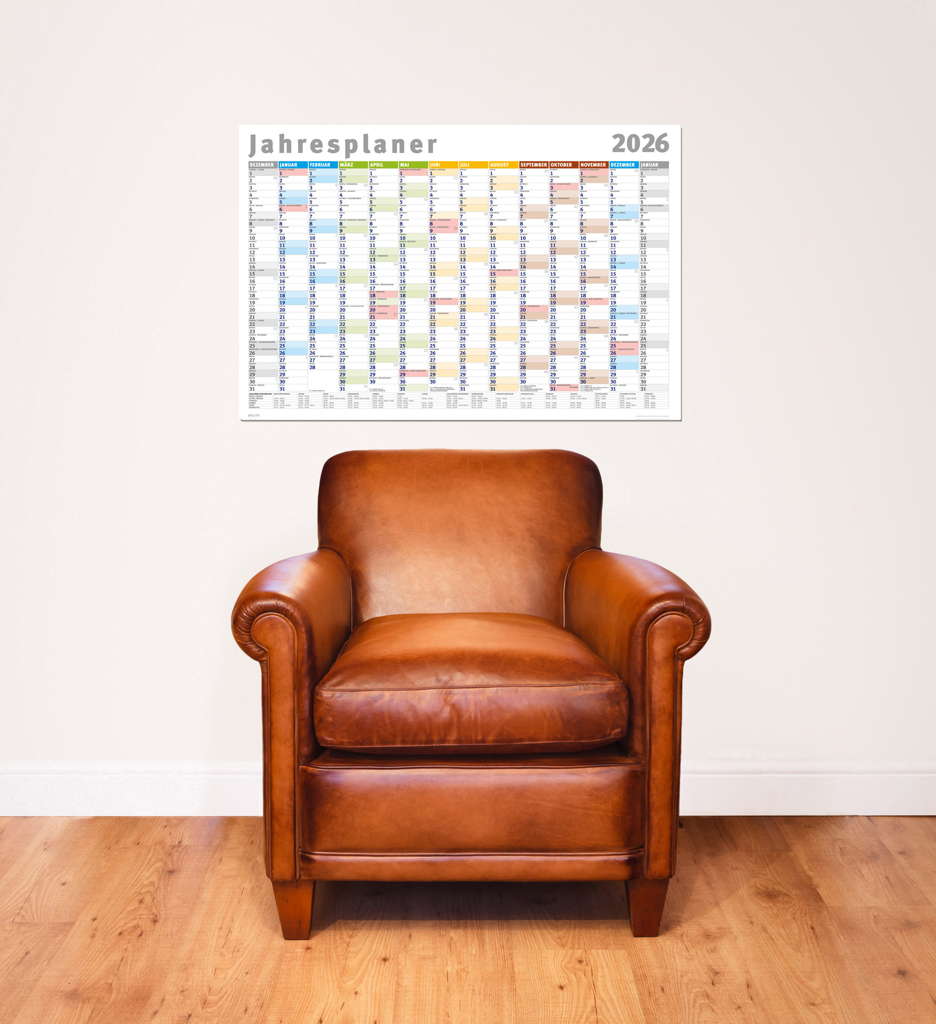 Ein brauner Ledersessel steht unter einem Kalender für 2026. Der Kalender hängt an einer weißen Wand, der Boden ist Holz.