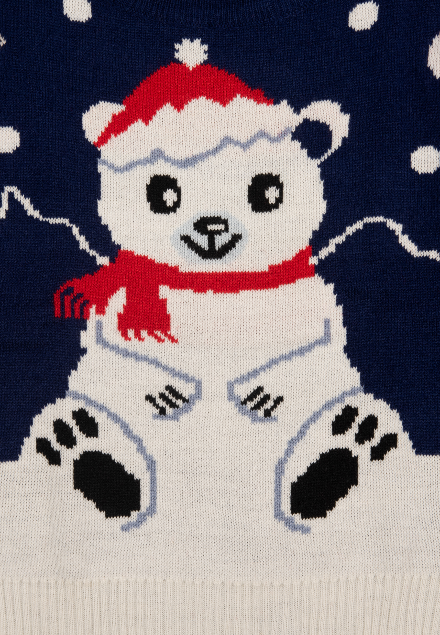 Ein Strickpullover mit Eisbärenmuster. Der Bär trägt einen roten Hut und Schal vor blauem Hintergrund.