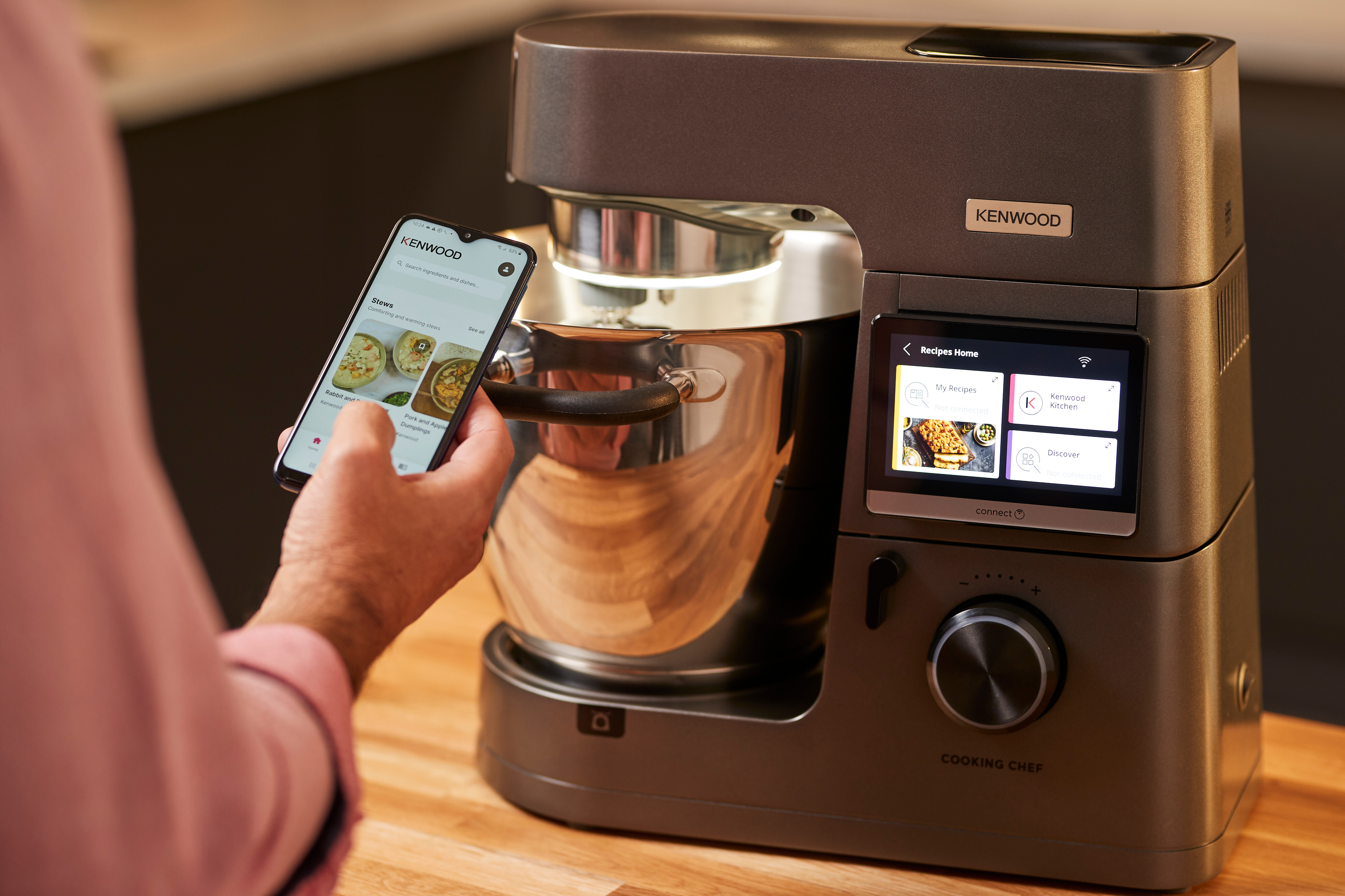 Eine Person hält ein Telefon mit Eintopf-Rezepten in der Nähe einer Kenwood Cooking Chef Maschine.