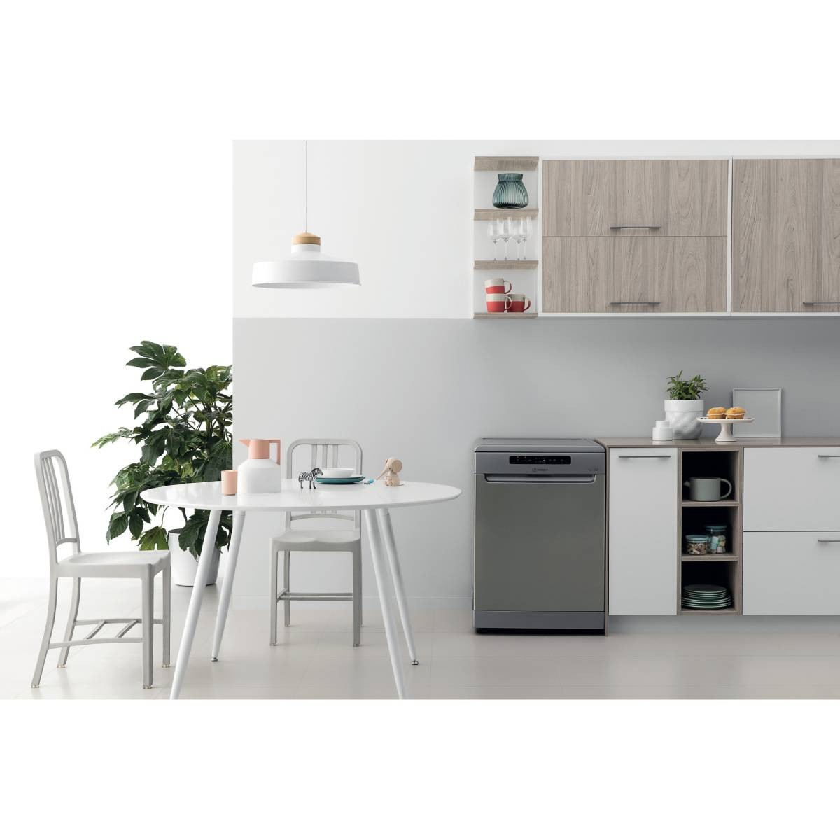 Interior de cocina con mesa redonda, sillas, lavavajillas y armarios. Se ven una planta, lámpara y vajilla.