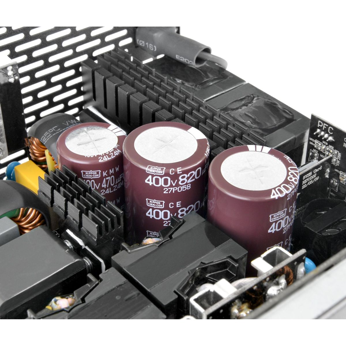 Primo piano di componenti elettronici, tra cui condensatori, dissipatori di calore e circuiti stampati. I condensatori sono cilindrici ed etichettati.
