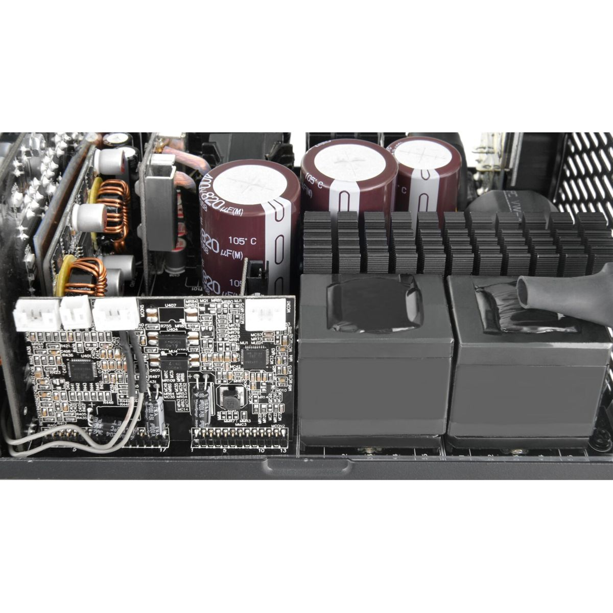 Interno di un alimentatore per computer. Condensatori, circuiti stampati e un dissipatore di calore nero visibili. Sono presenti vari componenti.
