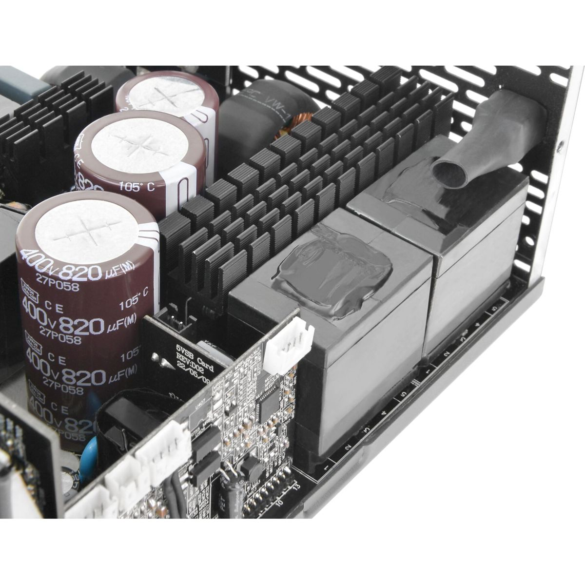 Primo piano di componenti elettronici, tra cui condensatori, un circuito stampato e dissipatori di calore neri, all'interno di un alimentatore.