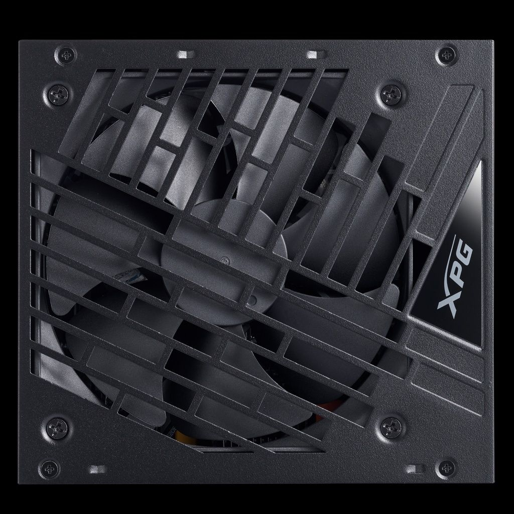 Een zwarte computer voeding met een ventilator achter een rooster. Het XPG-logo staat op de zijkant. Schroeven zijn zichtbaar.
