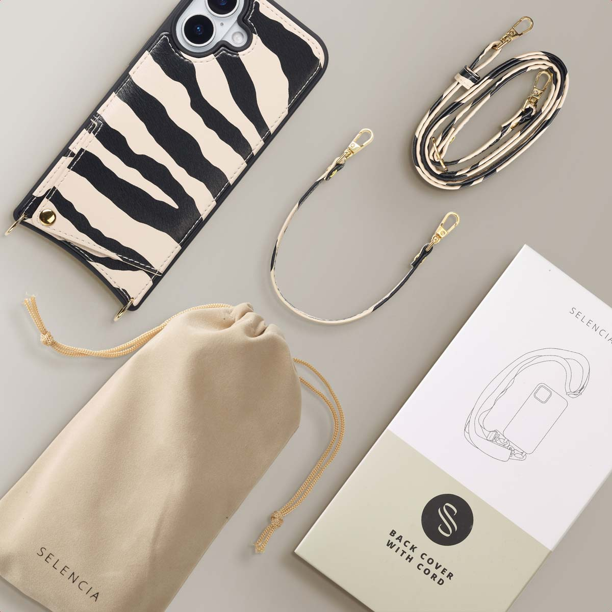 Een telefoonhoesje met zebrapatroon, een beige zakje, een riem en een doos met een illustratie van een telefoonhoesje op een grijze ondergrond.