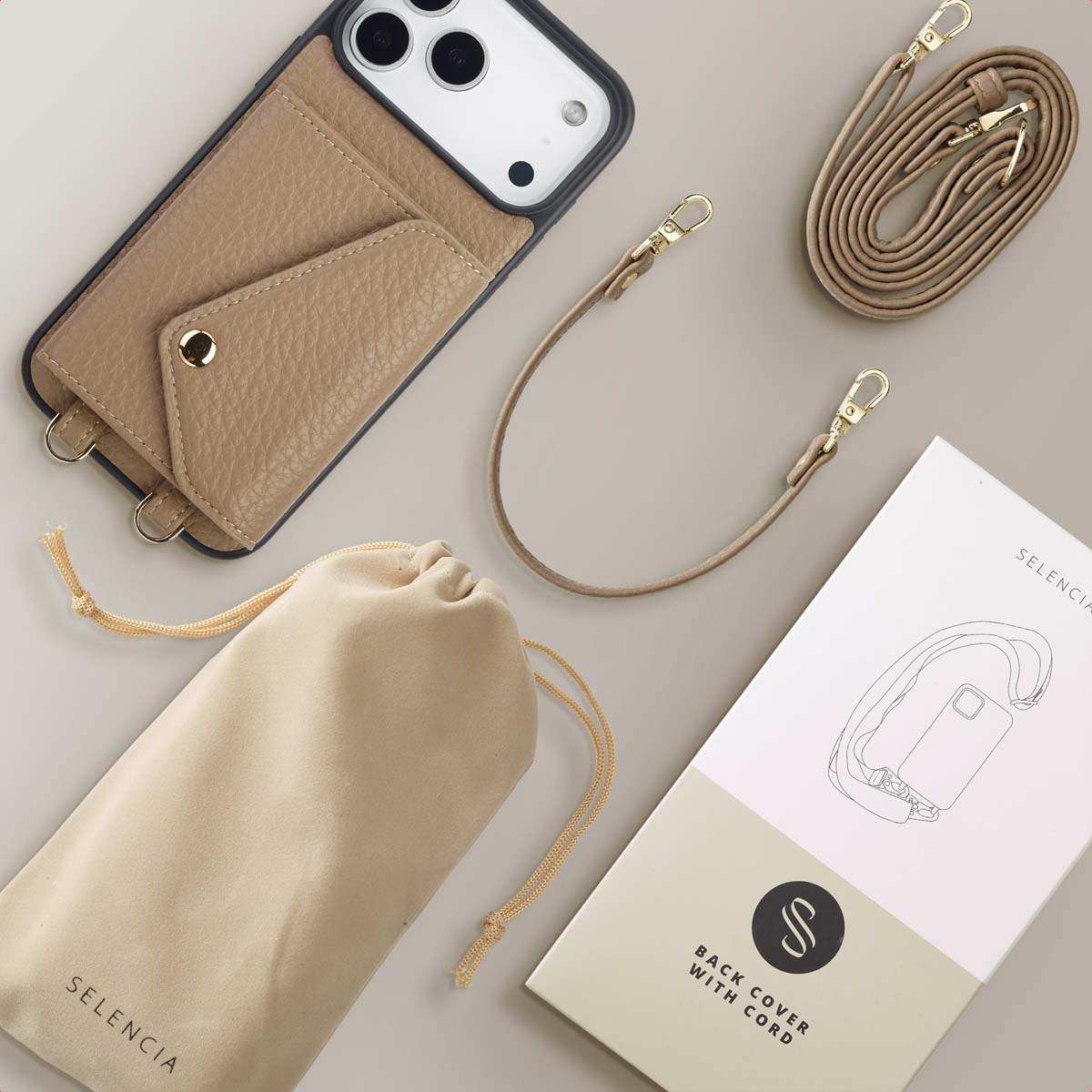 Coque de téléphone beige avec une sangle, une pochette, une boîte avec un schéma de coque et une sangle enroulée sur surface grise claire.