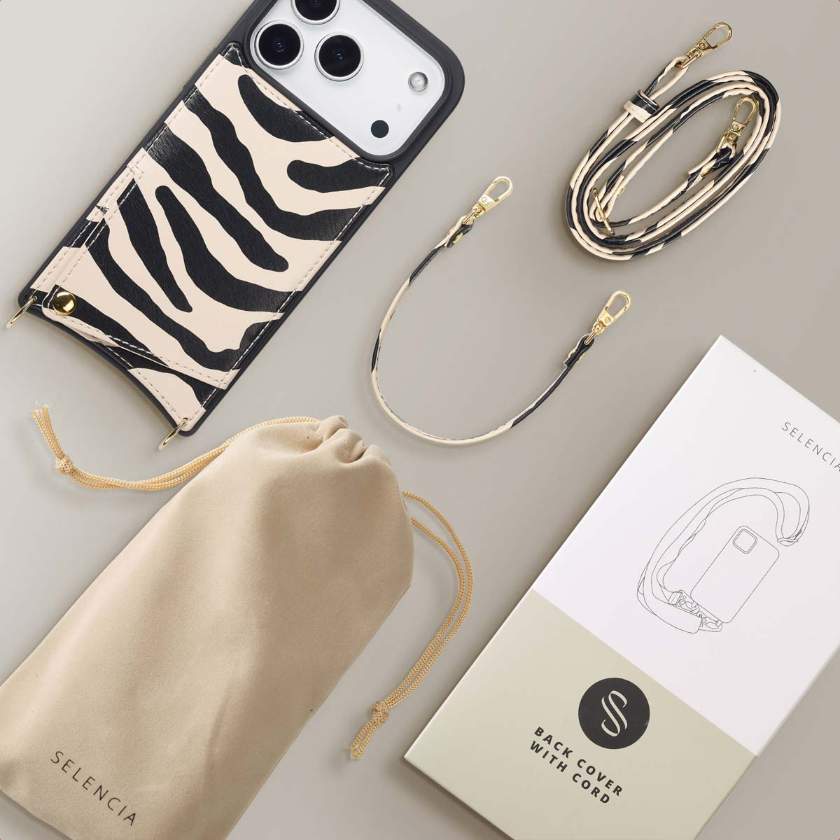 Une coque de téléphone à rayures zébrées, une sangle et une pochette sont disposées avec une boîte et une sangle plus courte sur une surface grise.