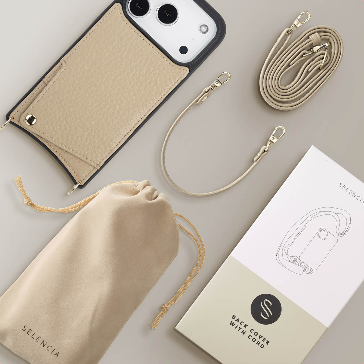 Een telefoonhoesje met een band, een zakje en een doos. Alles is beige. Het hoesje is aan de band bevestigd. Op de doos staat 'Back cover with cord'.