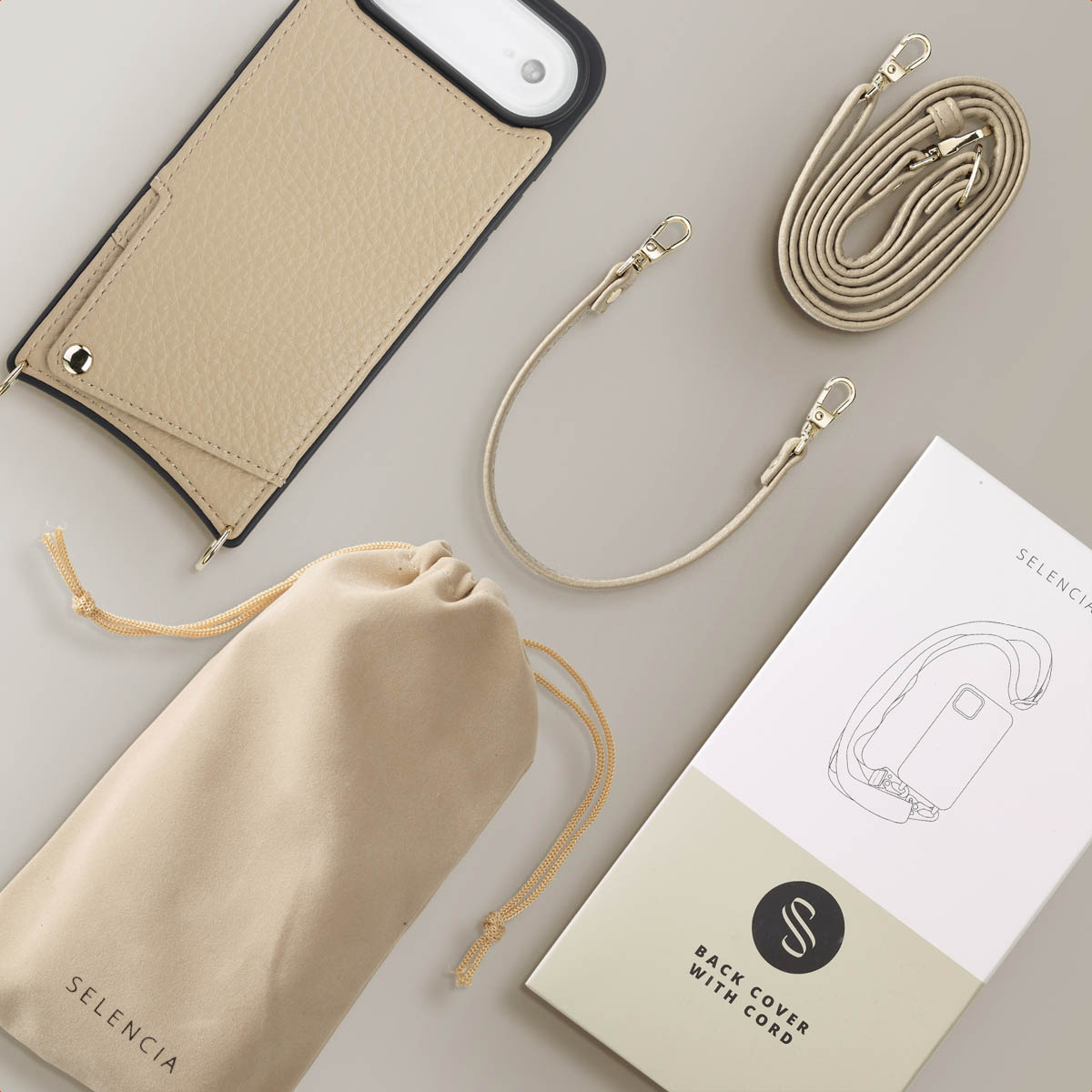 Étui de téléphone beige avec sangle, pochette et emballage sur une surface grise. L'étui est à côté d'une sangle enroulée et d'un livret.
