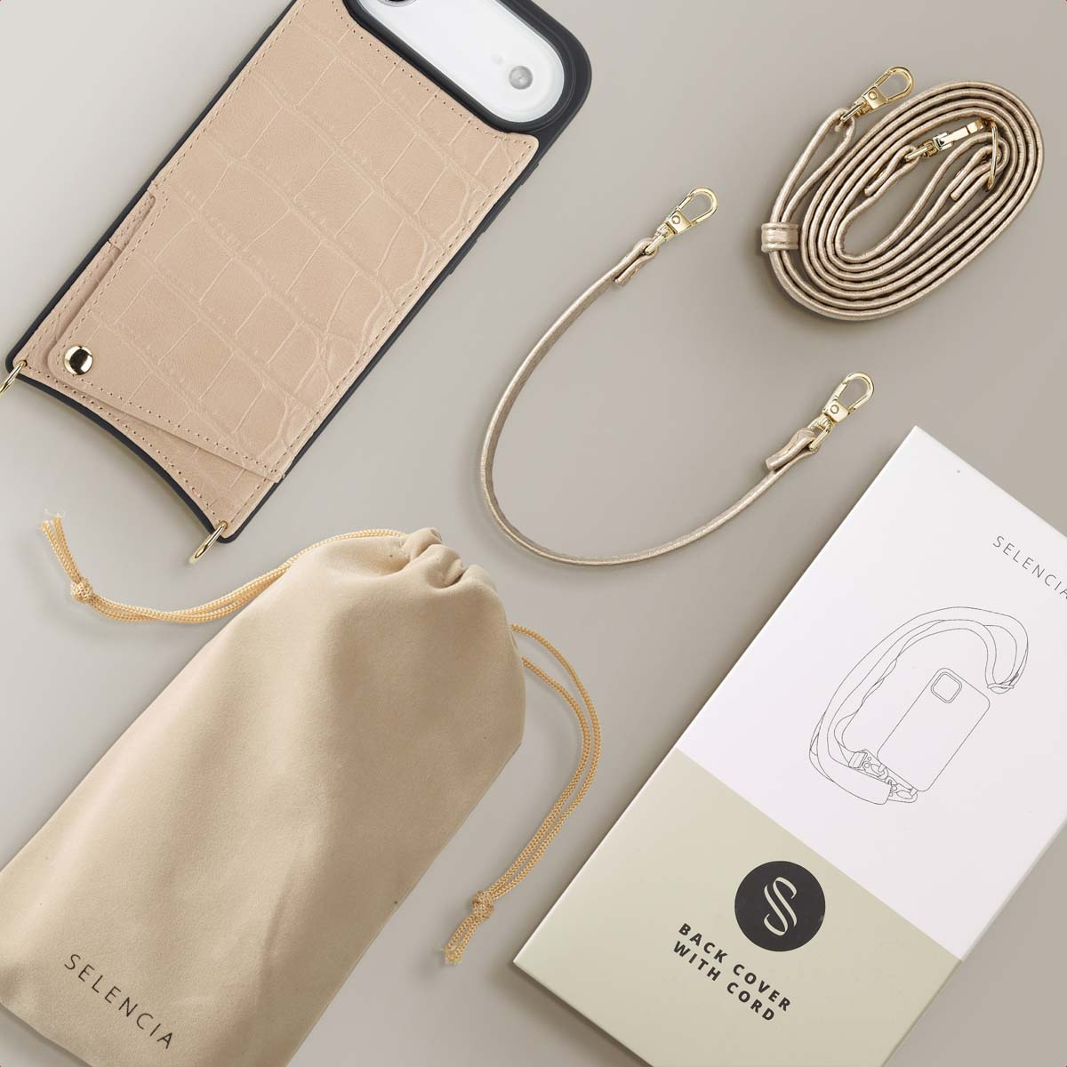 Coque de téléphone beige avec sangle, pochette et boîte, le tout sur une surface grise. Quincaillerie et détails dorés visibles.