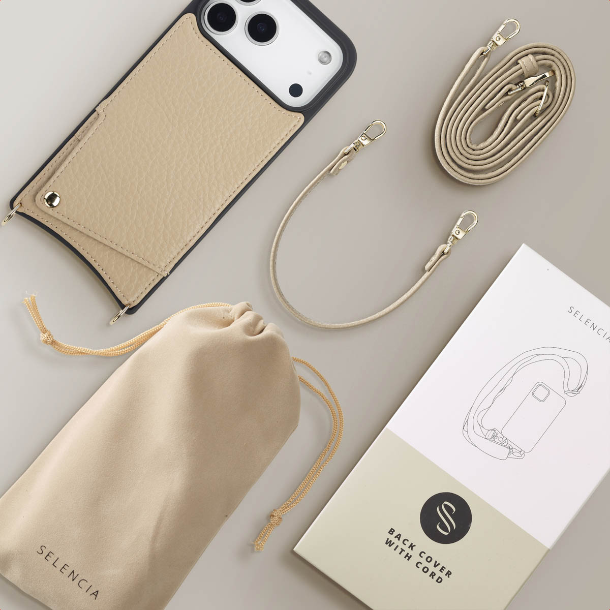 Beige telefoonhoesje met kaarthouder, afneembare riem, etui en verpakking. Alle items liggen op een lichtgrijze ondergrond.