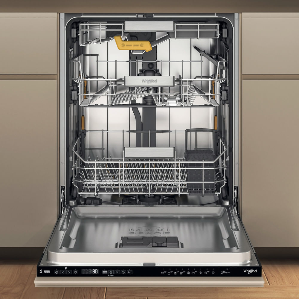 Una lavastoviglie Whirlpool aperta. Interno argentato con ripiani, un porta utensili giallo e pannello di controllo. Ante di armadi beige sullo sfondo.
