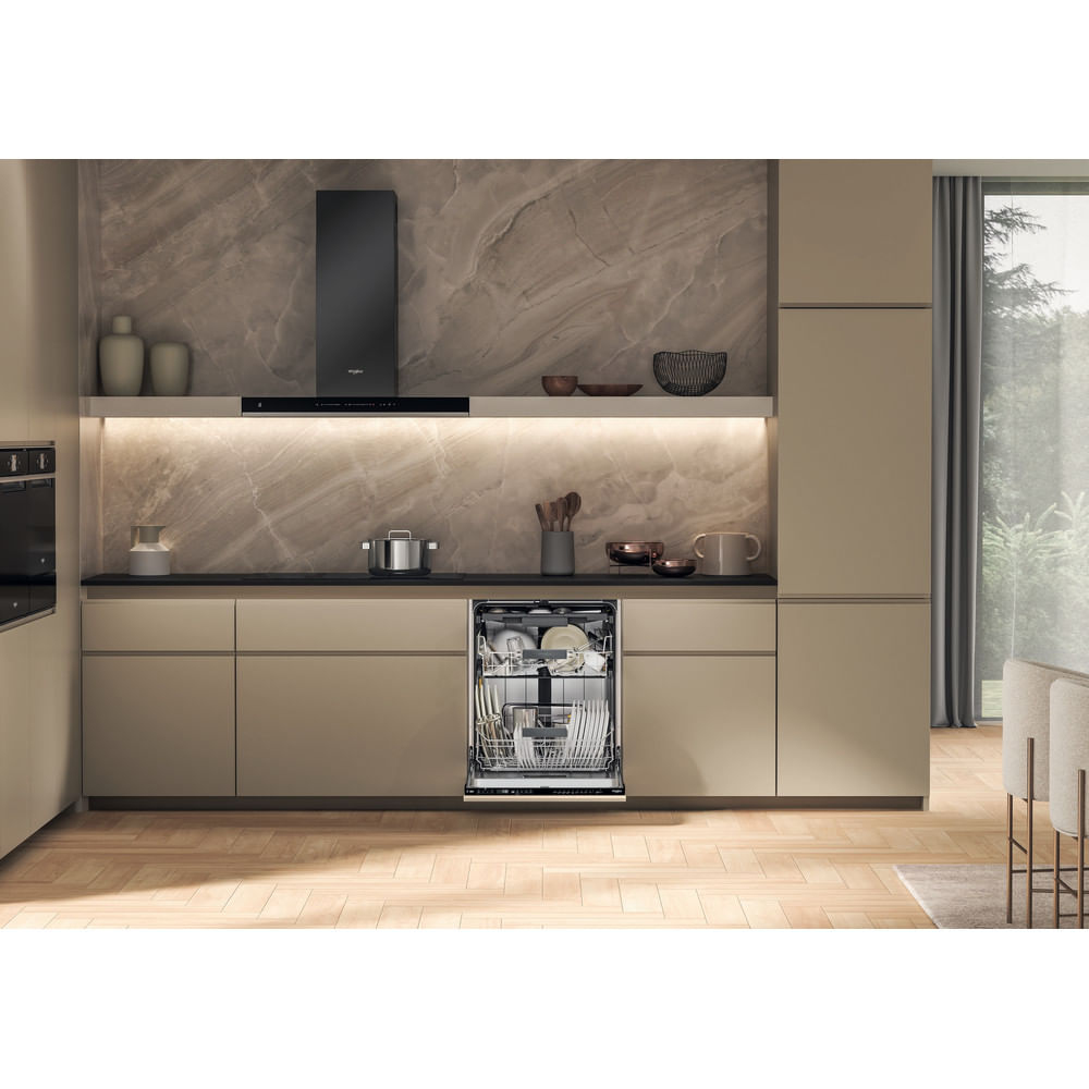 Cucina moderna con lavastoviglie aperta. Armadi beige, alzatina in marmo, cappa nera e pavimento in legno. Piatti all'interno della lavastoviglie.