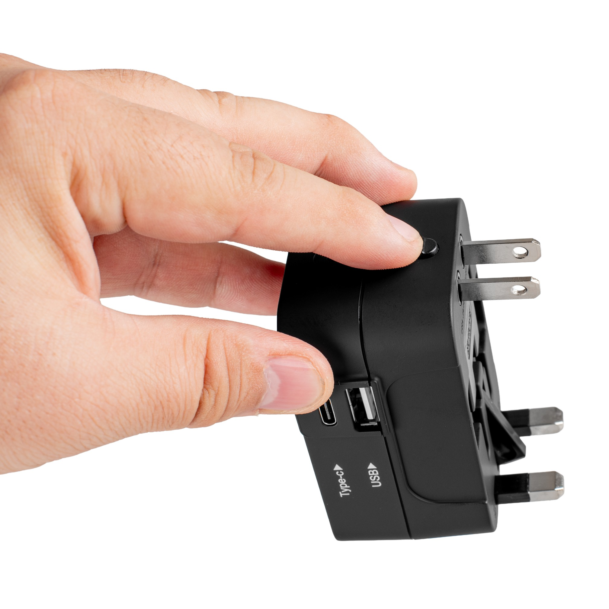 Dłoń trzyma czarną przejściówkę podróżną z portami USB i Type-C oraz wieloma typami wtyczek na białym tle.