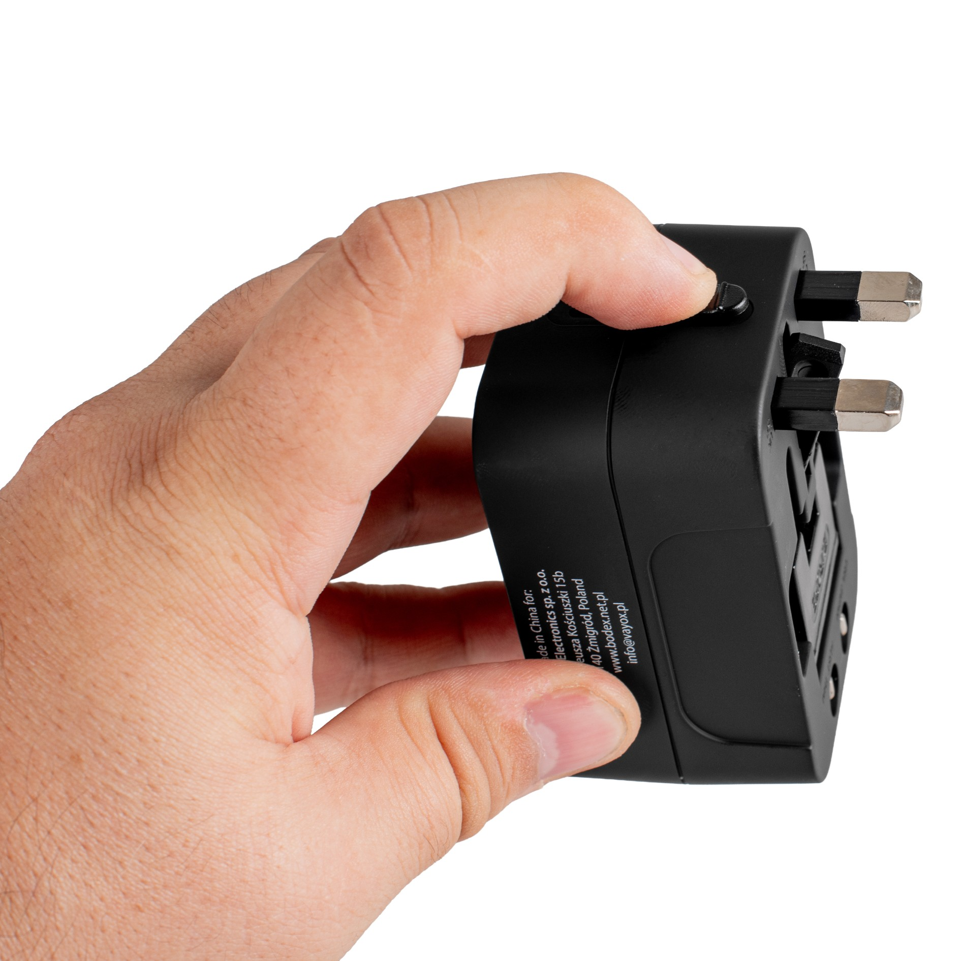 Ręka trzyma czarny adapter podróżny. Adapter ma wtyczki i przycisk. Białe tło.