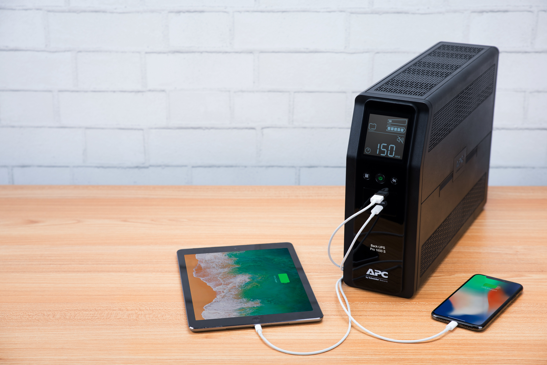 Un UPS nero carica un tablet e un telefono. Il tablet e il telefono mostrano schermate di ricarica. Cavi bianchi collegano i dispositivi.