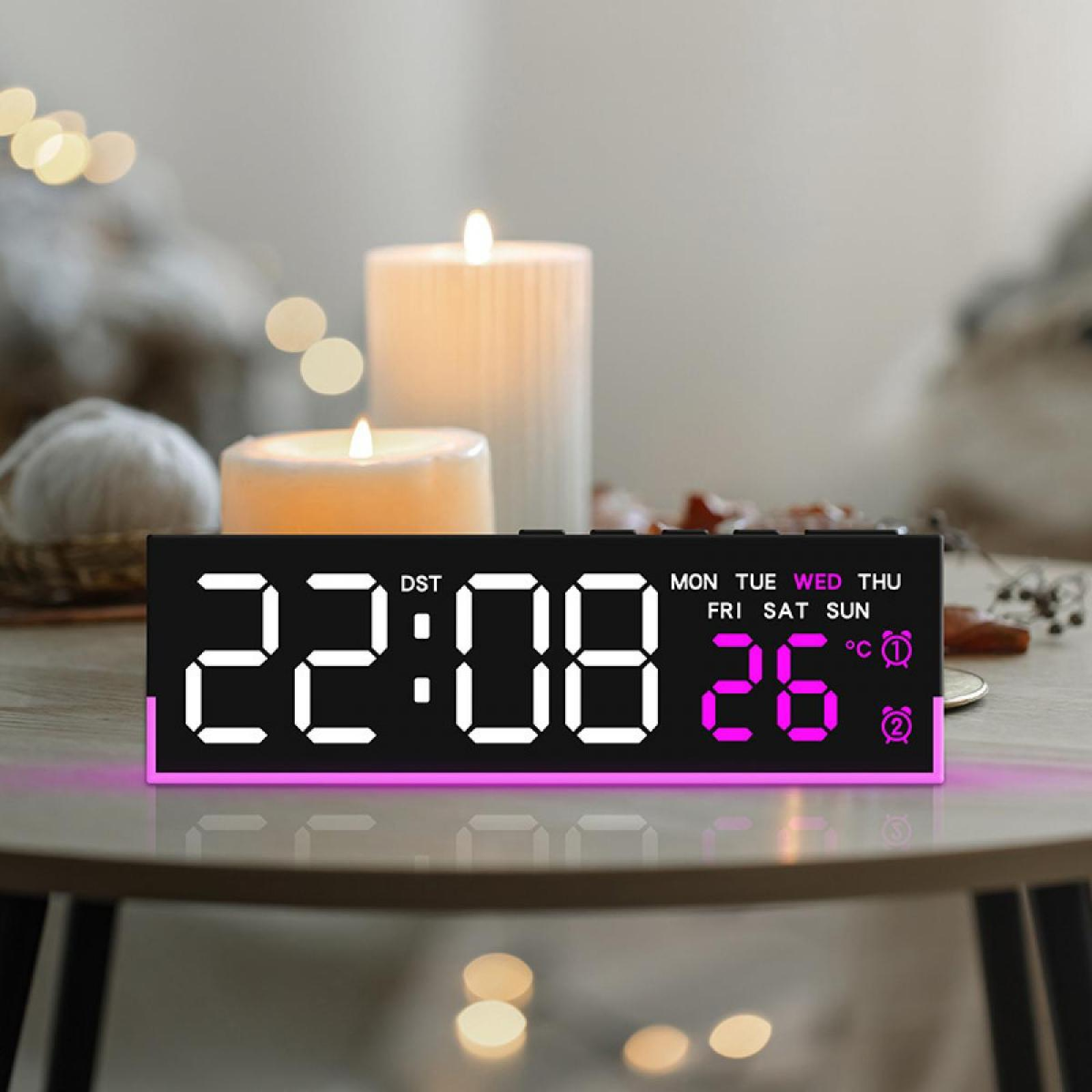 Eine Digitaluhr zeigt 22:08, Datum 26. Zwei Kerzen und ein verschwommener Hintergrund sind sichtbar.