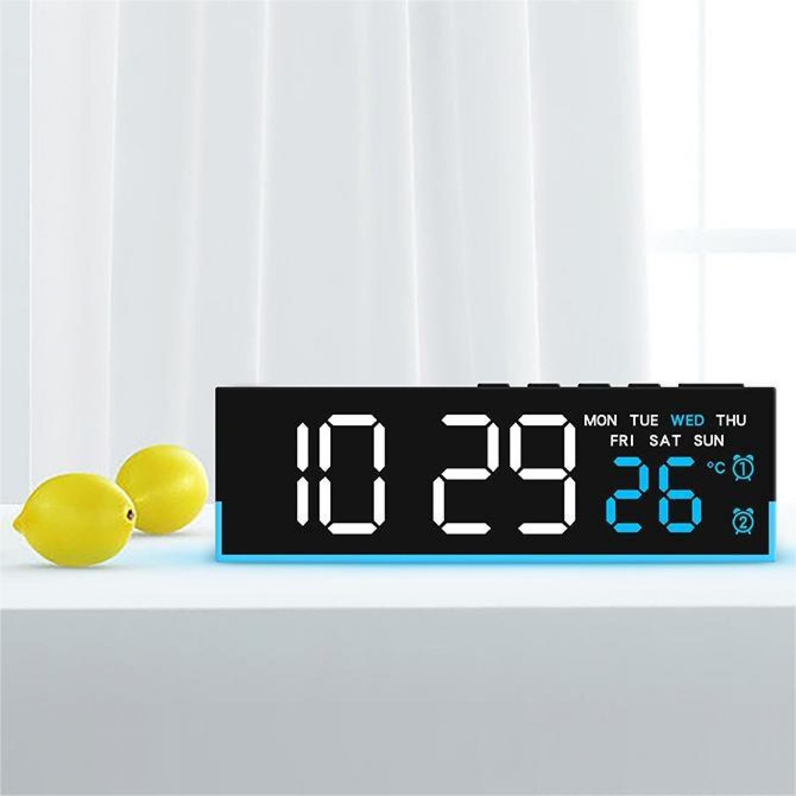 Eine Digitaluhr zeigt 10:29:26 mit Tag und Temperatur an. Zwei gelbe Zitronen liegen daneben auf einer weißen Oberfläche.