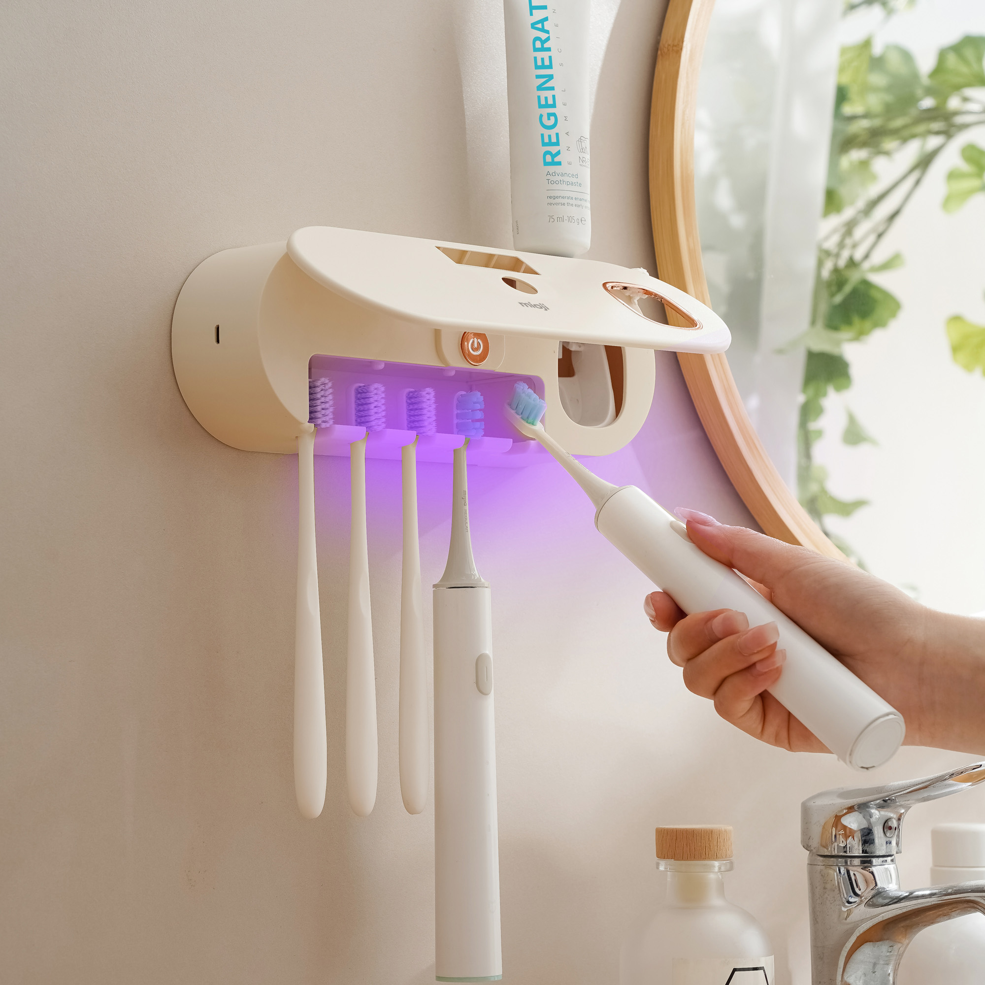 Duvar üzerinde bir diş fırçası tutucusunun yakınında bir elektrikli diş fırçası tutan bir kişi. Tutucuda birkaç diş fırçası var.
