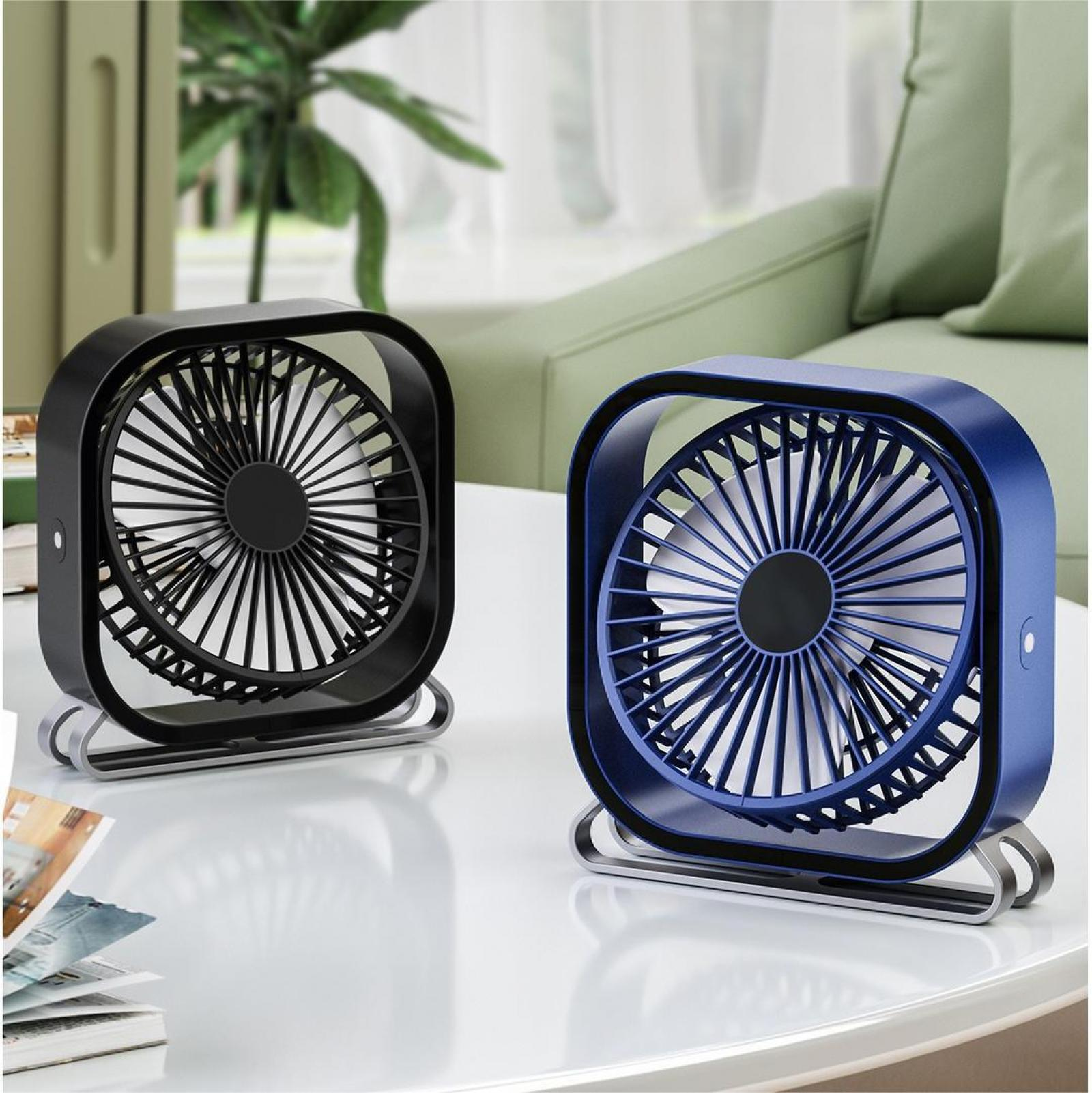 Zwei kleine Ventilatoren, einer schwarz und einer blau, stehen auf einem weißen Tisch. Dahinter sind ein Sofa und ein Fenster.