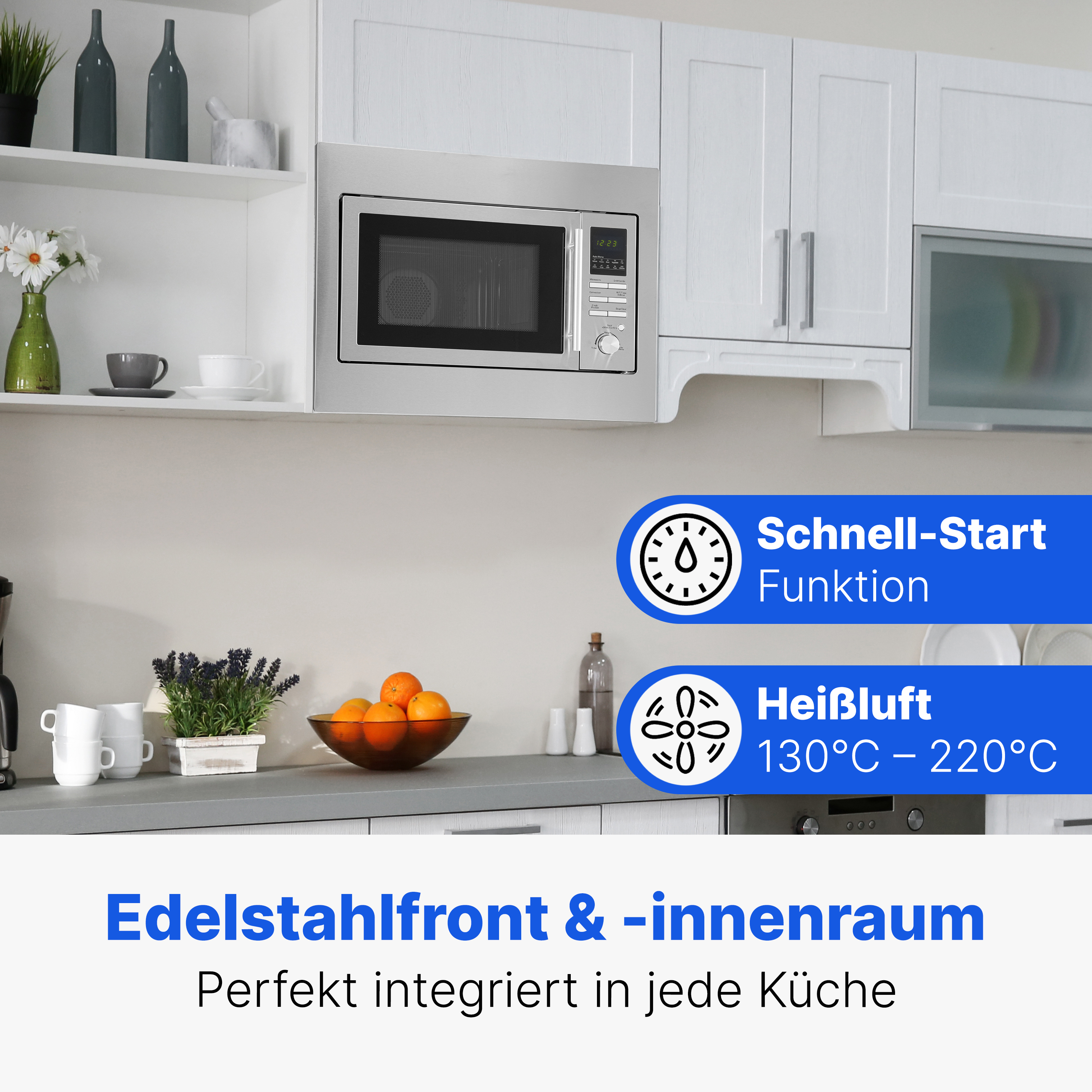 Eine moderne Küche mit Mikrowelle. Es gibt weiße Schränke und Regale mit Küchenutensilien. Orangen und Blumen sind sichtbar.