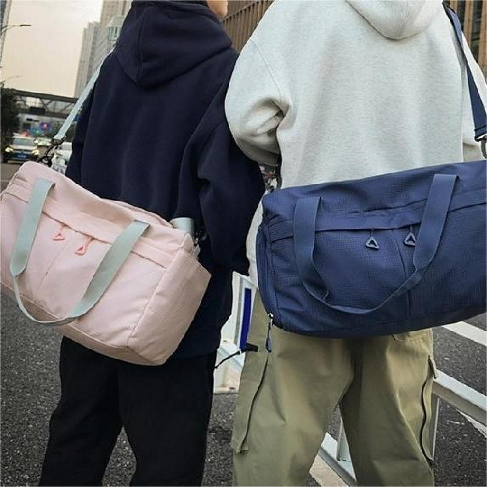 Zwei Personen mit Reisetaschen. Einer hat eine rosa Tasche, der andere eine blaue Tasche. Sie tragen Hoodies und stehen auf einer Straße.