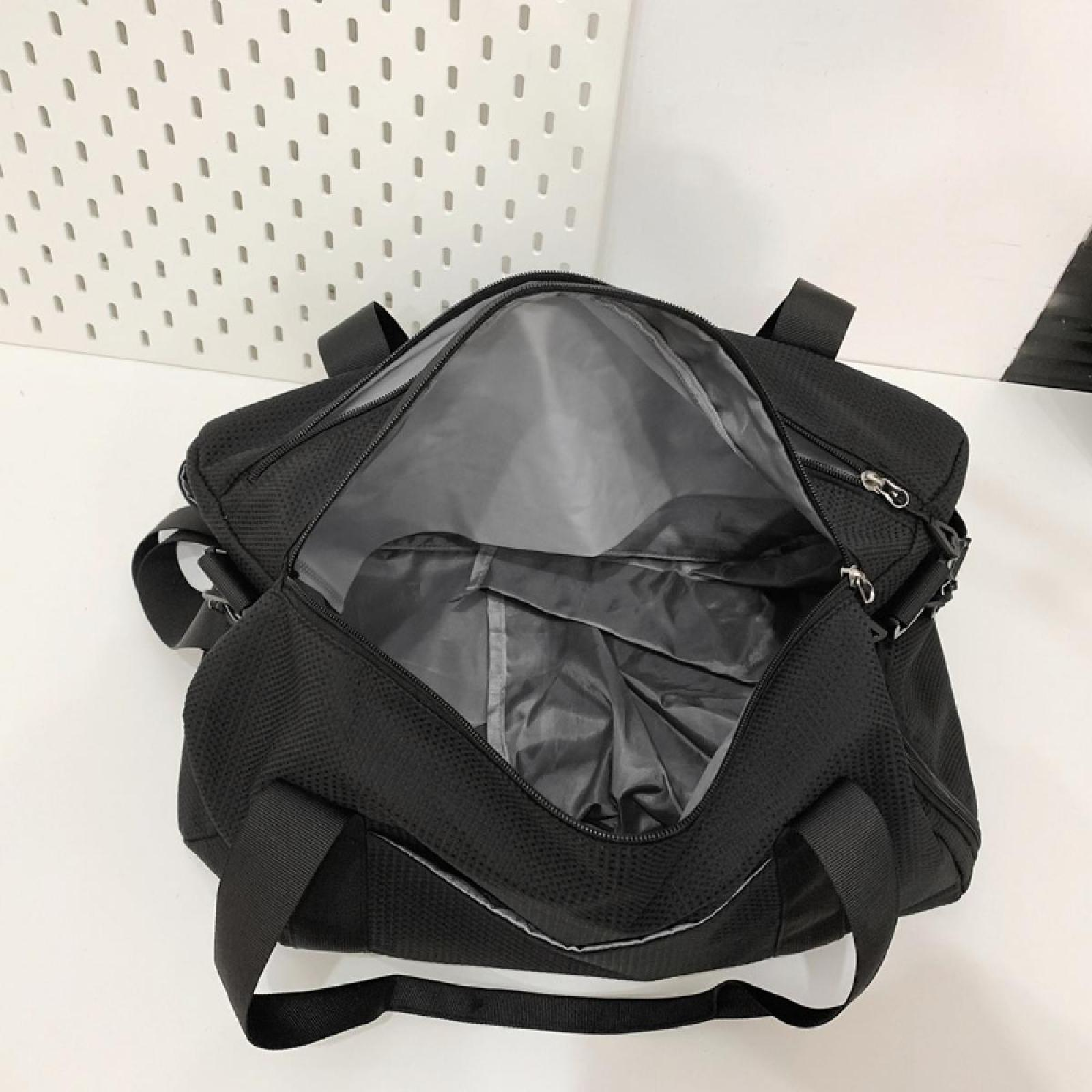 Offene schwarze Reisetasche mit grauem Innenraum auf weißer Oberfläche. Hintergrund ist eine weiße Wand mit Löchern.