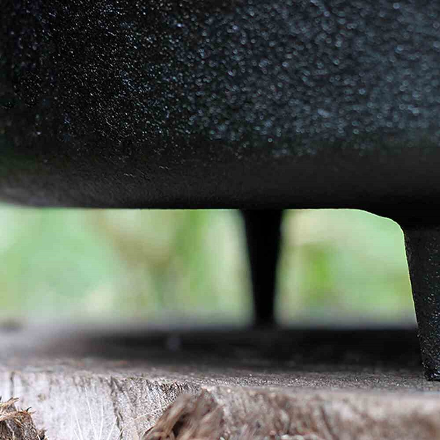 Zbliżenie czarnego żeliwnego garnka na drewnianej powierzchni z zielonymi liśćmi w tle.