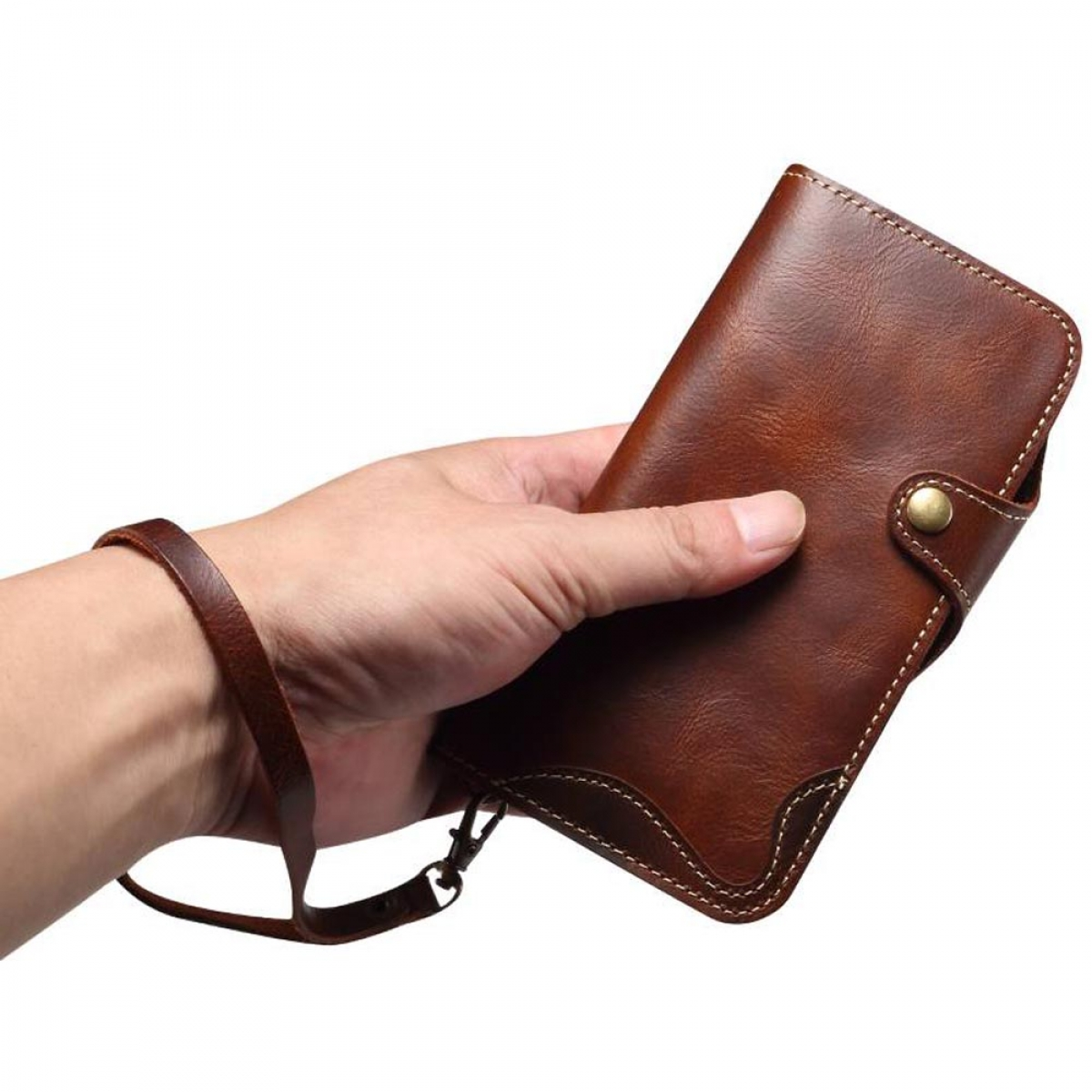 Eine Hand hält eine braune Lederbrieftasche mit einer Handschlaufe. Die Brieftasche hat einen Knopfverschluss und weiße Nähte.