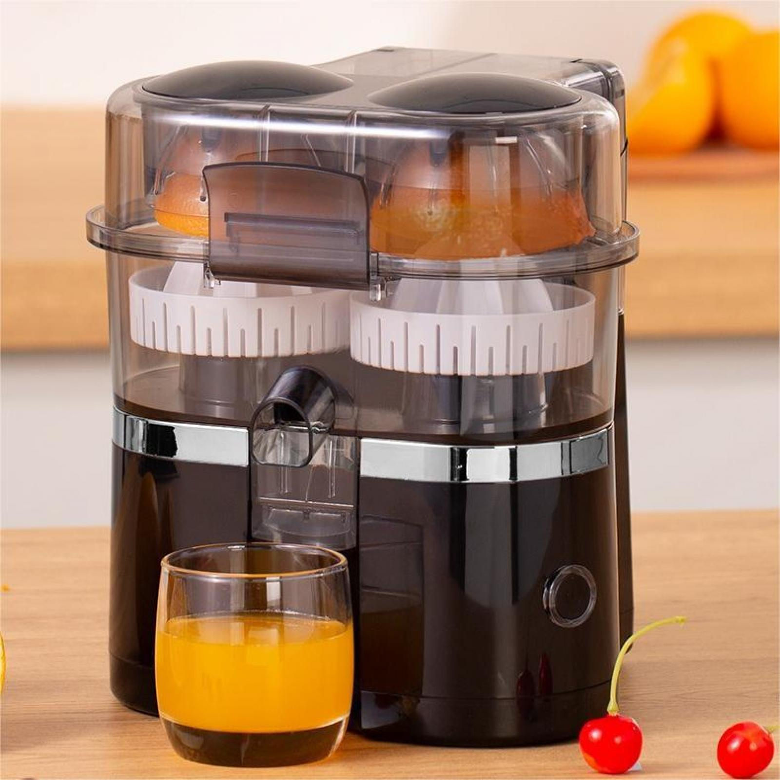 Ein Entsafter mit Orangen im Inneren und einem Glas Saft davor. Zwei Kirschen sind rechts. Der Entsafter ist schwarz und transparent.