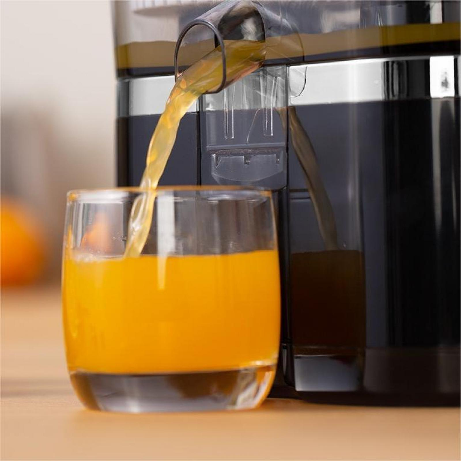 Saft gießt in ein Glas. Rechts ist eine Saftpresse. Das Glas ist mit Orangensaft gefüllt. Der Hintergrund ist verschwommen.