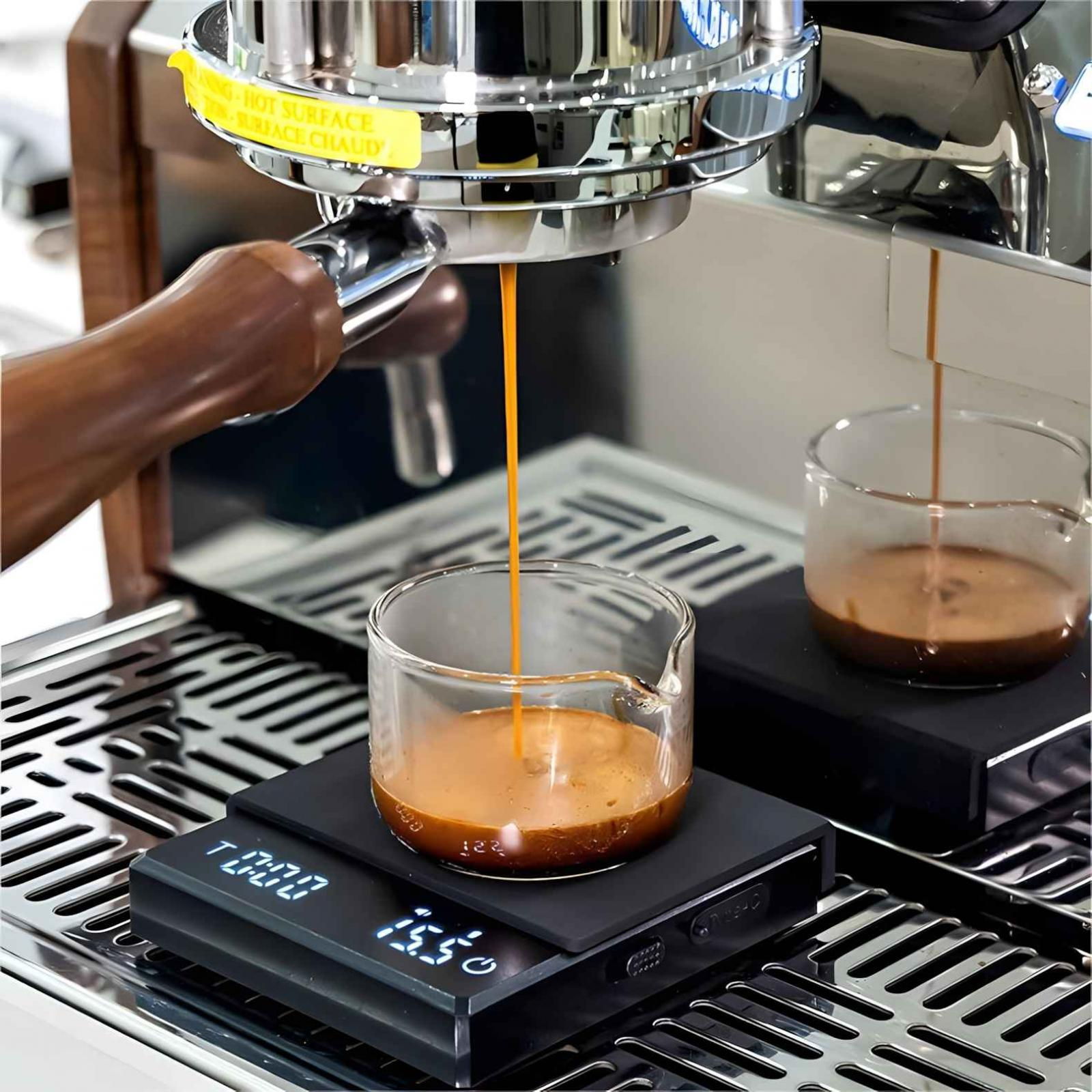 Espressomaschine gibt Kaffee in ein Glas ab. Eine Waage zeigt 15,5 g. Ein anderes Glas hat Kaffee.
