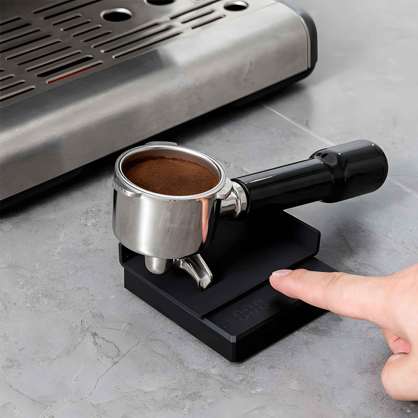 Ein Espressomaschinen-Siebträger mit Kaffee liegt auf einer schwarzen Waage. Eine Hand drückt eine Taste. Im Hintergrund ist die Maschine.