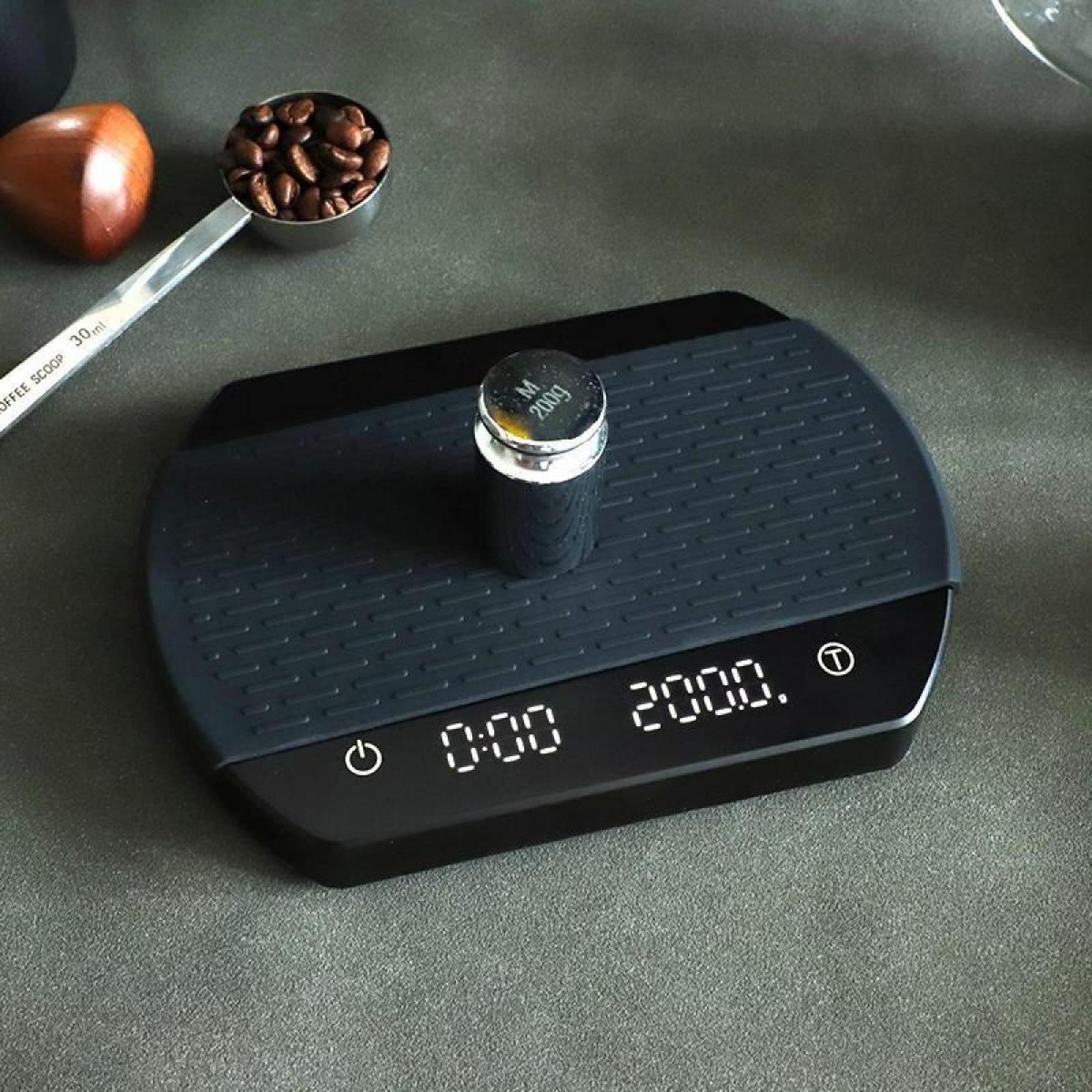 Eine digitale Küchenwaage mit einem Gewicht oben. Auf der Seite eine Schaufel mit Kaffeebohnen und ein Holzobjekt.