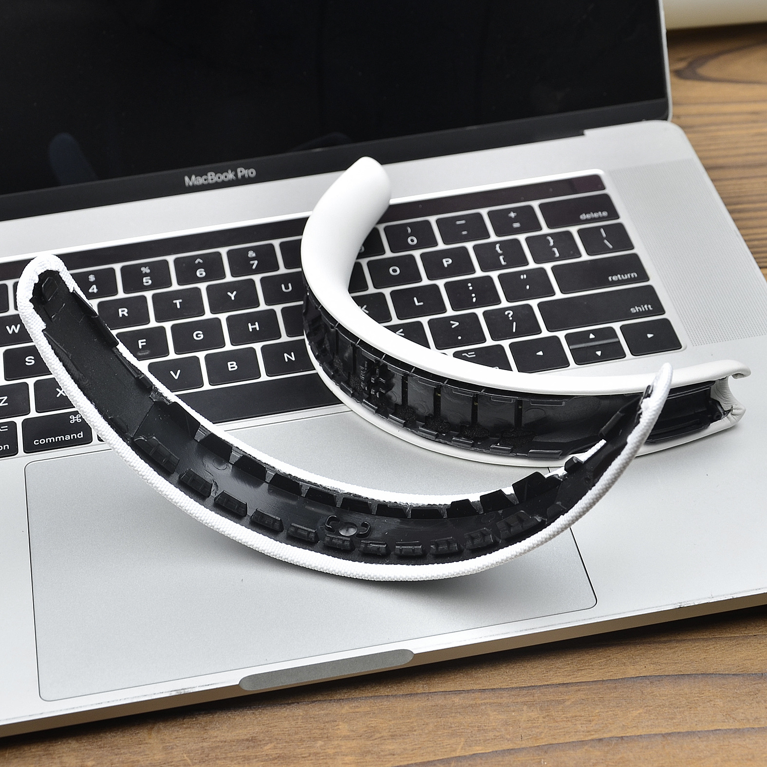 Dwa biało-czarne elementy zestawu słuchawkowego spoczywają na klawiaturze MacBooka Pro. Drewniana powierzchnia w tle.