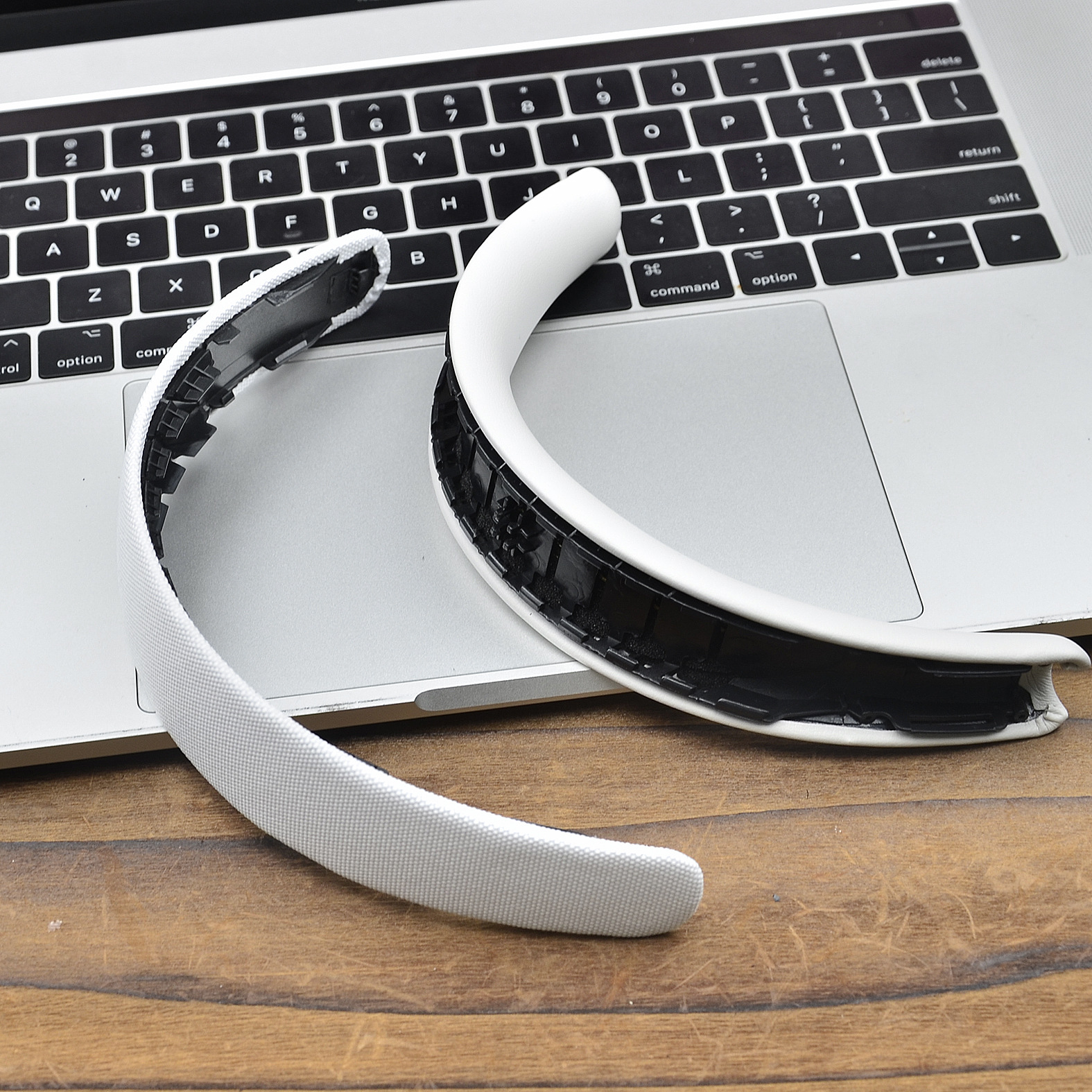 Białe, zakrzywione urządzenie spoczywa na klawiaturze laptopa. Jest częściowo rozebrane, odsłaniając wewnętrzne, czarne elementy.