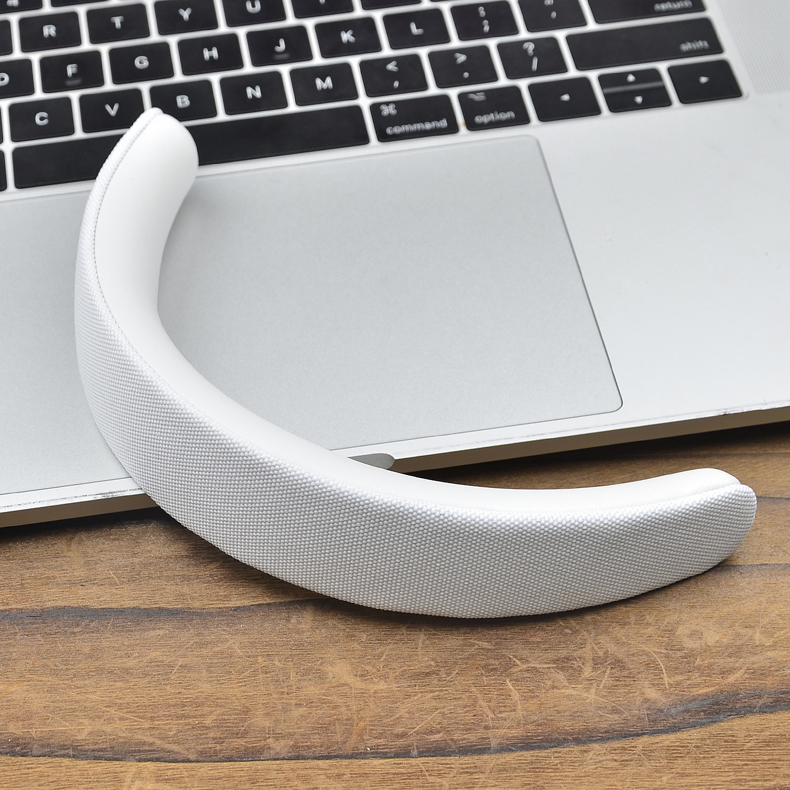 Biały głośnik na szyję spoczywa na laptopie, nad klawiaturą i gładzikiem, na drewnianym stole.